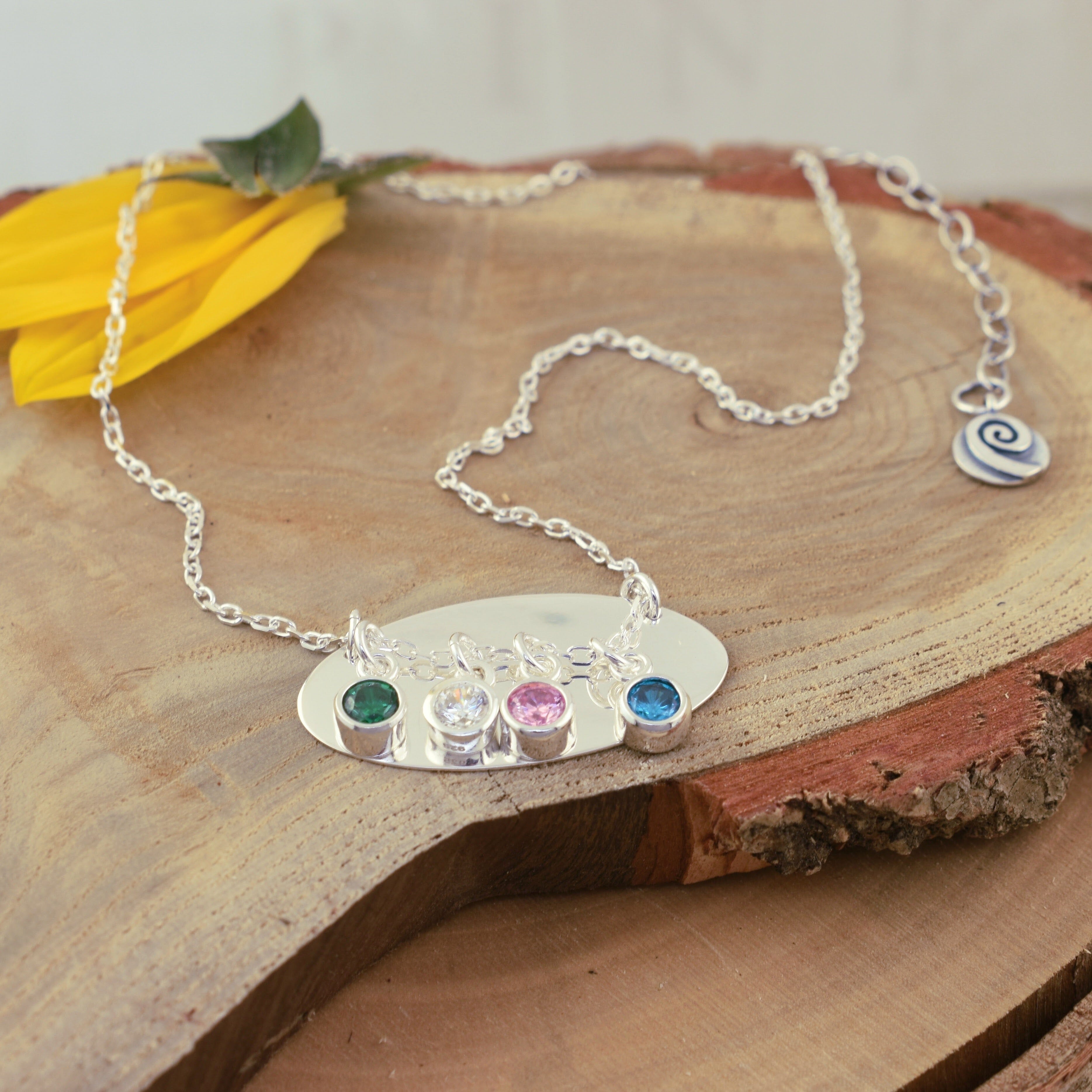 customizable birthstone sliding necklace on top of a plain silver oval disk