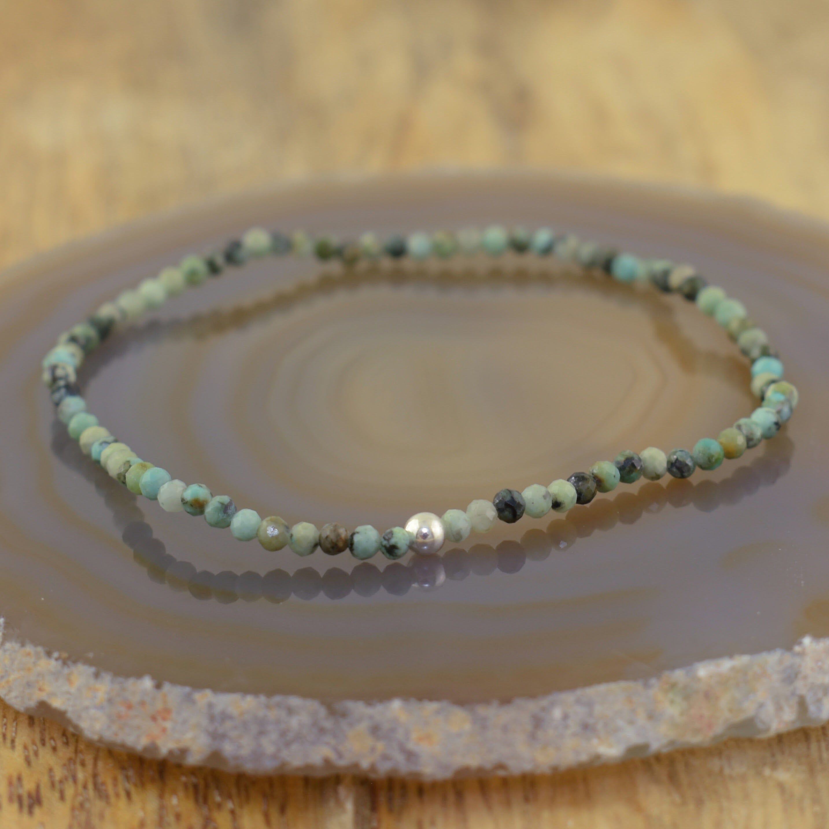 a beaded stretch bracelet made of small natural stone beads in shades of green, teal, and earthy tones, featuring a single polished silver bead accent