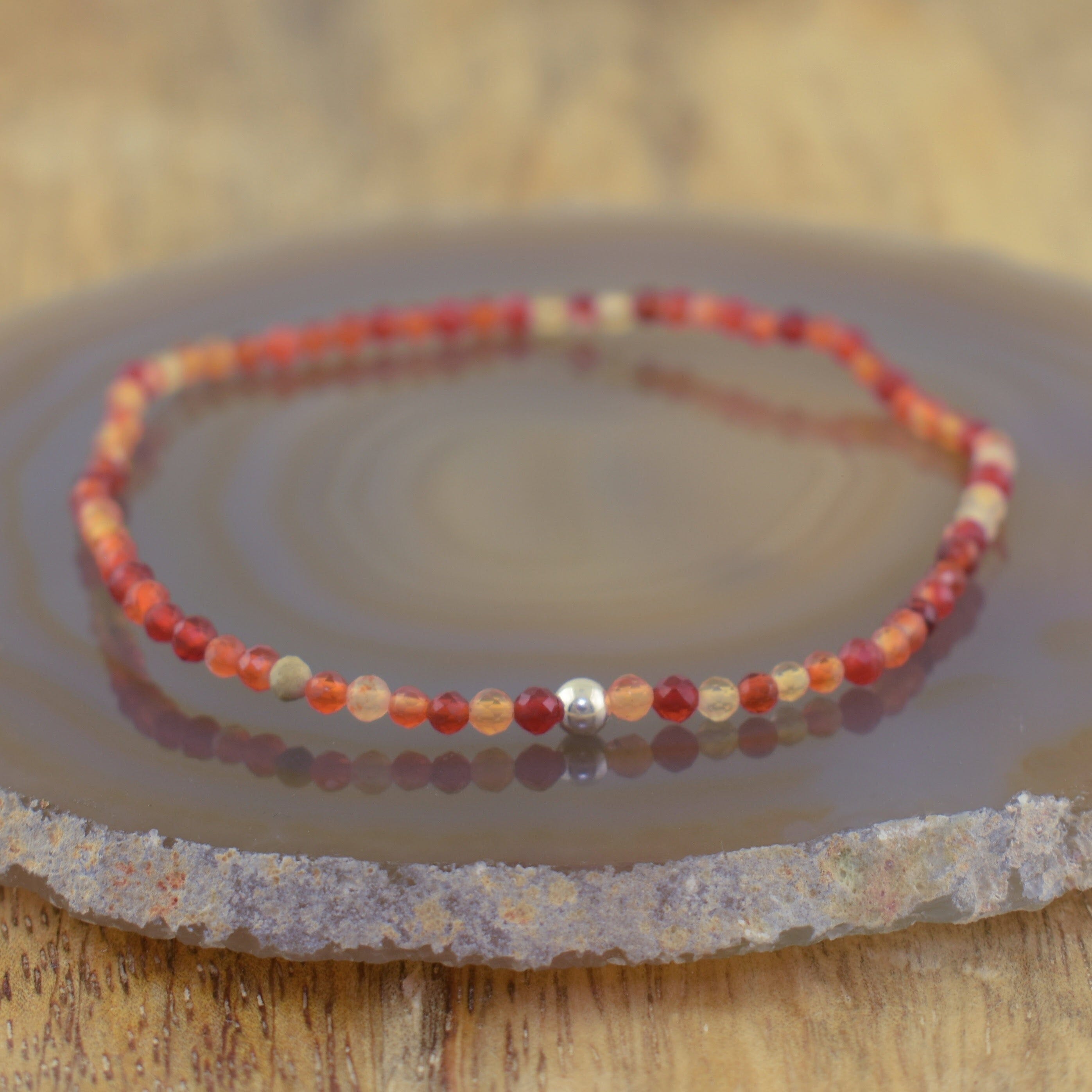 a beaded stretch bracelet made of small red, orange, and translucent beige beads with a single silver bead accent