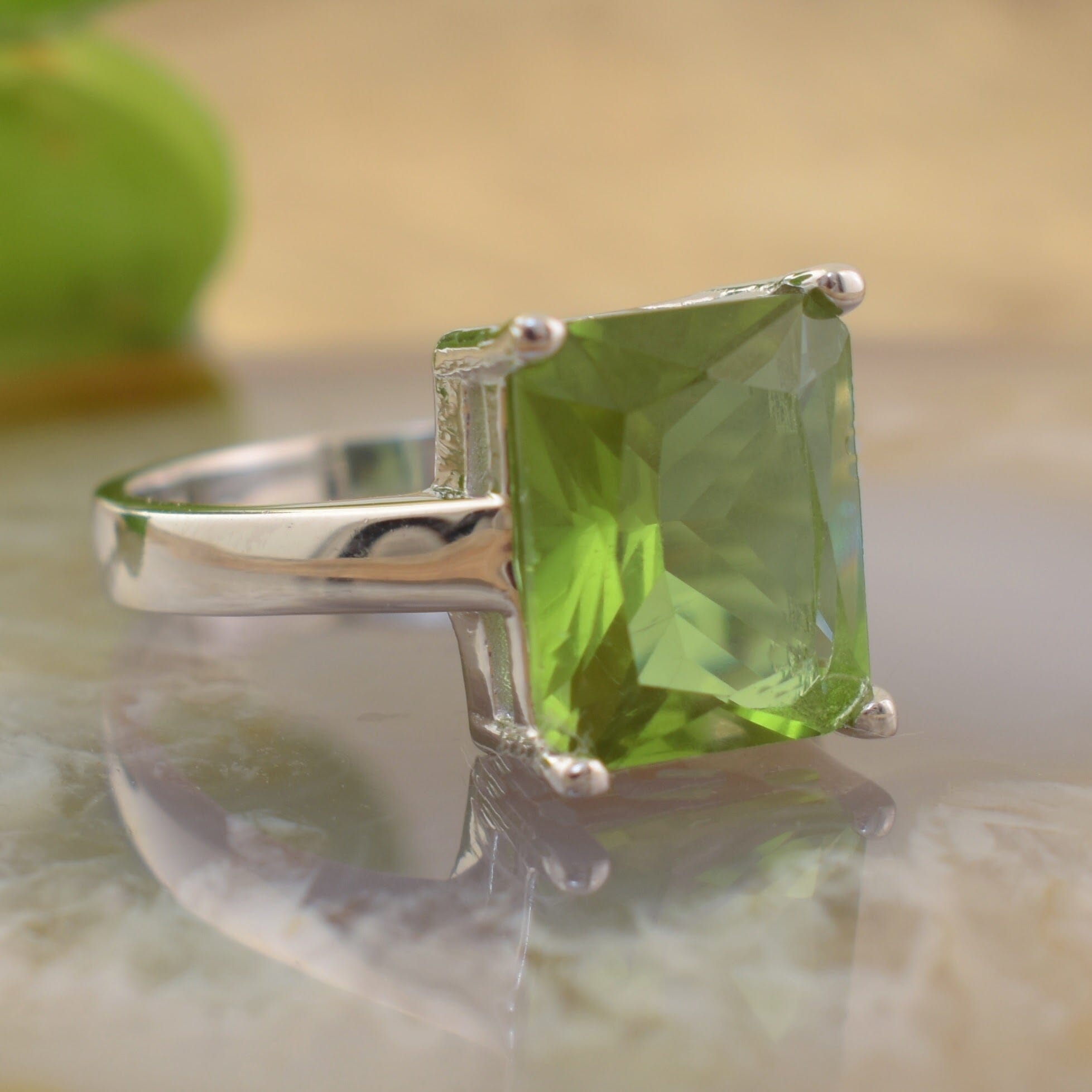 A sterling silver ring featuring a large, faceted green gemstone in a rectangular prong setting