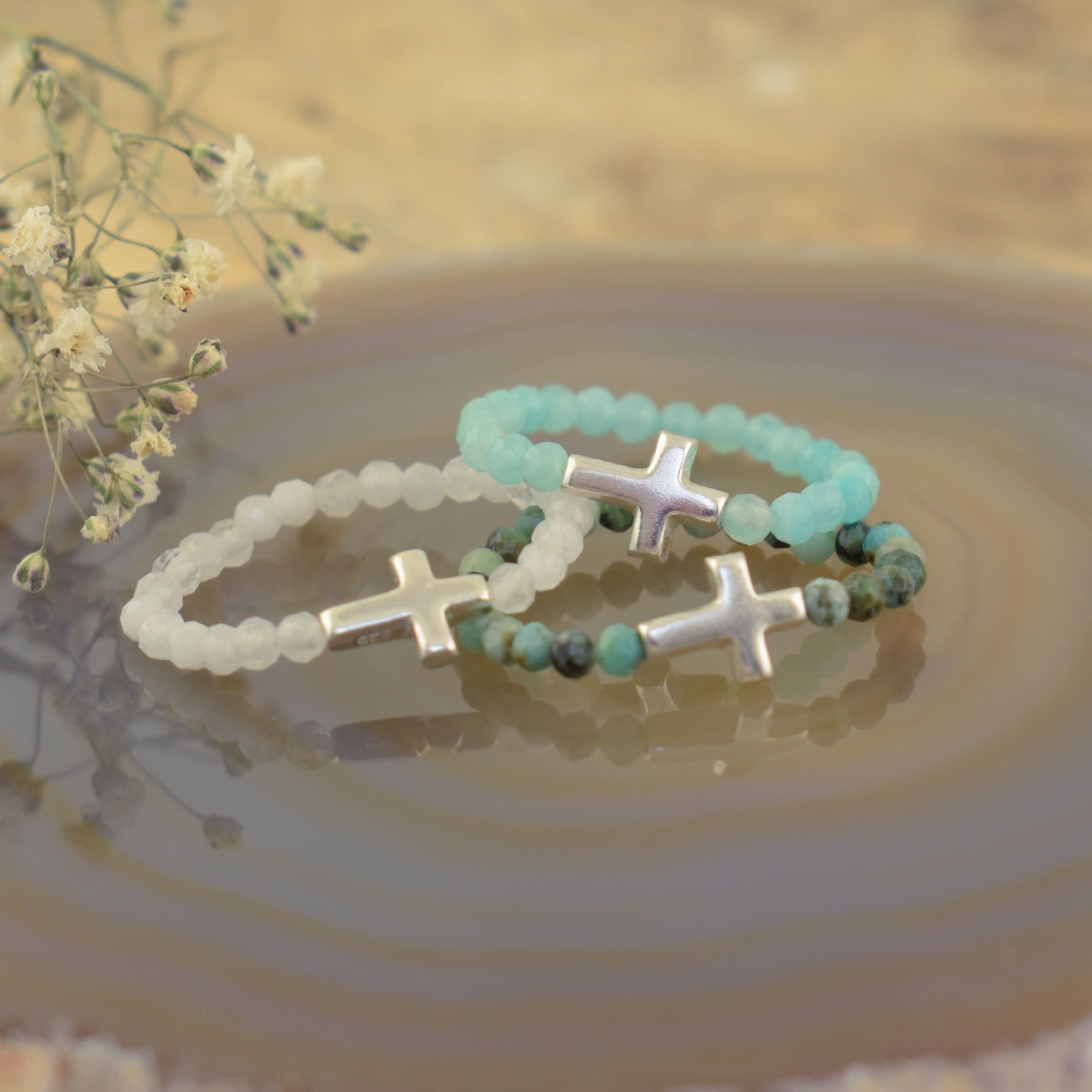 Three beaded stretch rings with silver cross charms, one bracelet is white, one is light aqua blue, and one features marbled green and white beads with a silver cross