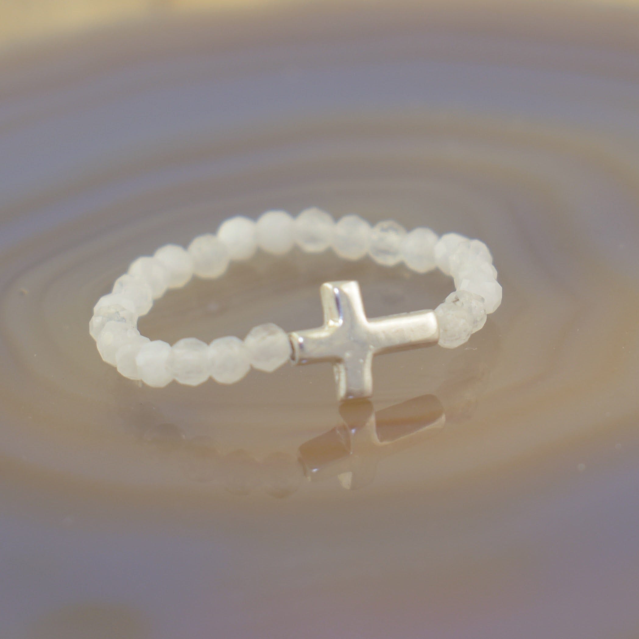 a beaded ring featuring translucent white round beads and a polished silver cross charm