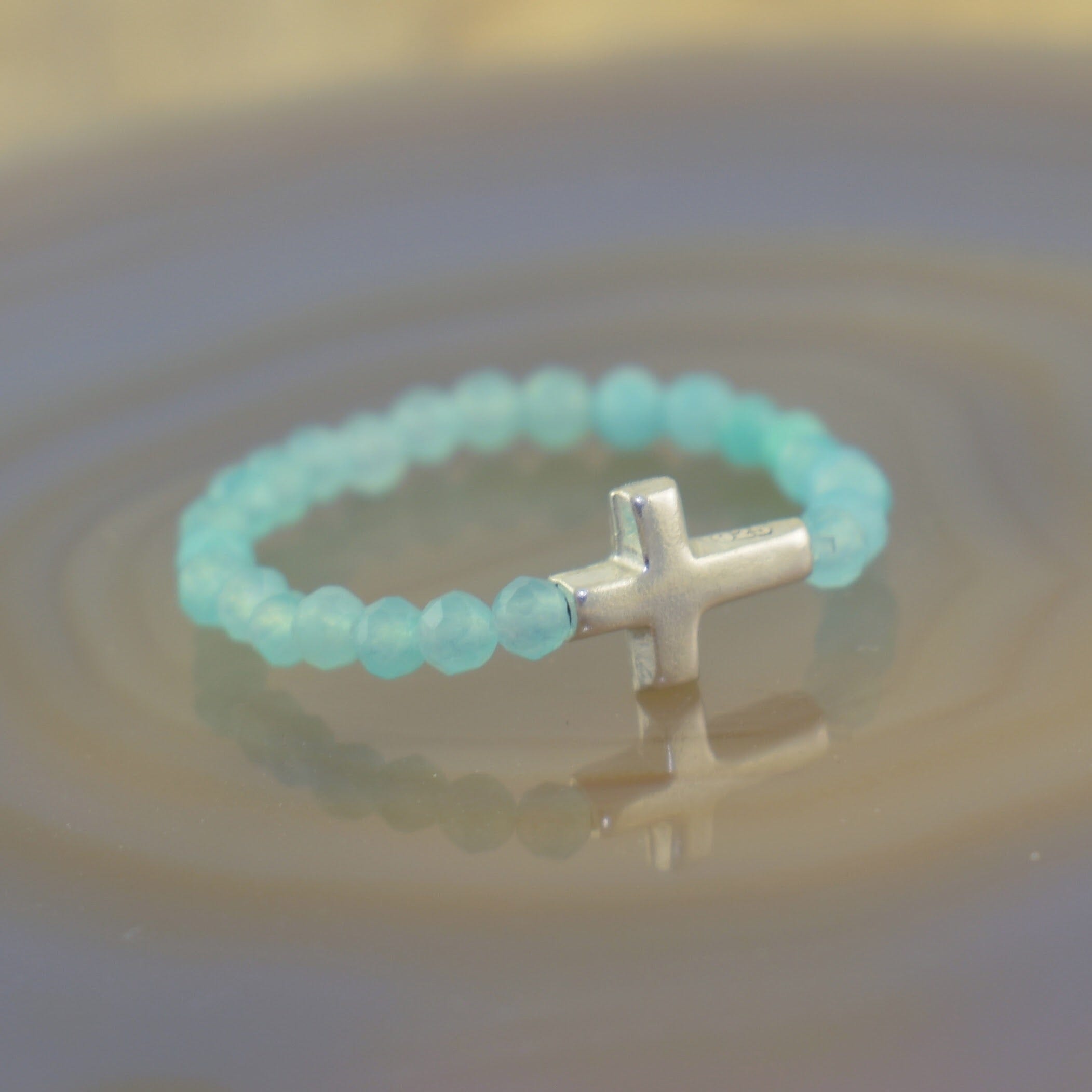a beaded ring featuring translucent light blue beads and a polished silver cross charm