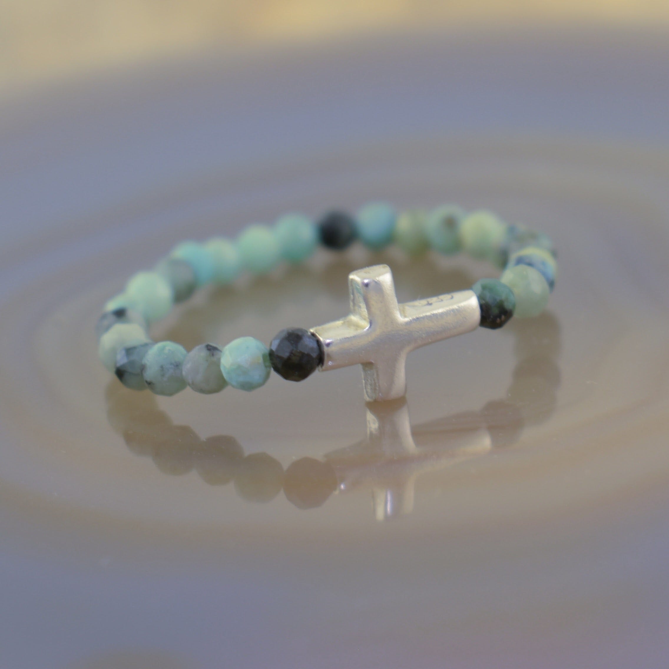 a beaded ring featuring light blue-green turquoise beads and a small silver cross centerpiece
