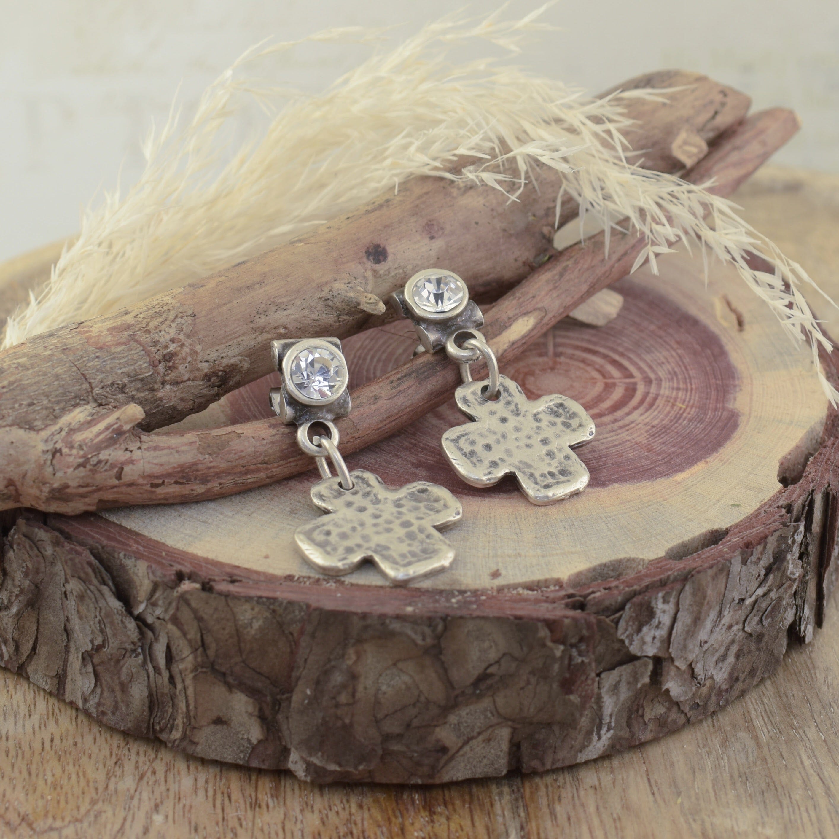 a pair of silver-toned posh boutique earrings, on a clear round CZ post, with a textured cross-shaped charm hanging.