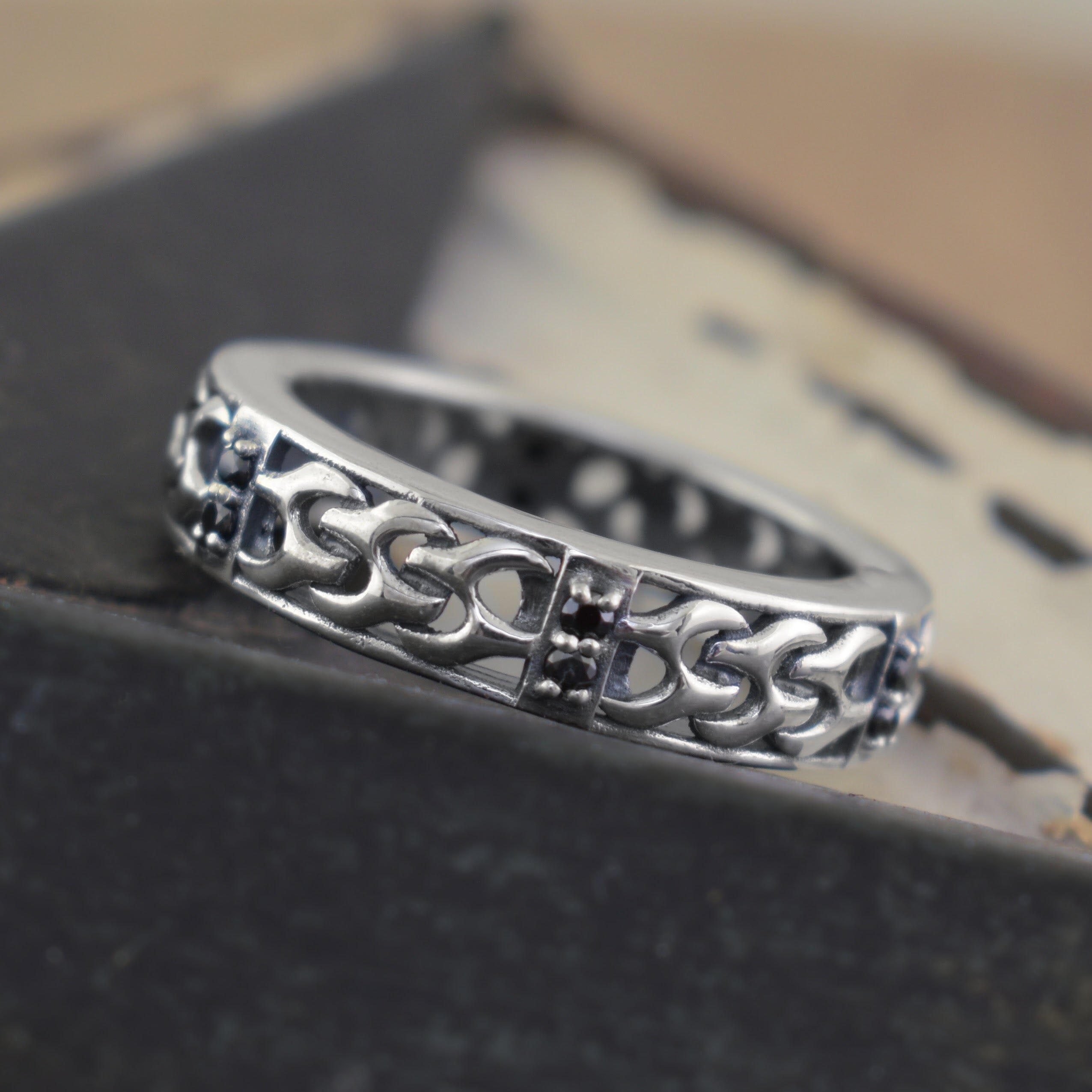 A sterling silver ring with an intricate Celtic knot pattern and small black gemstone accents