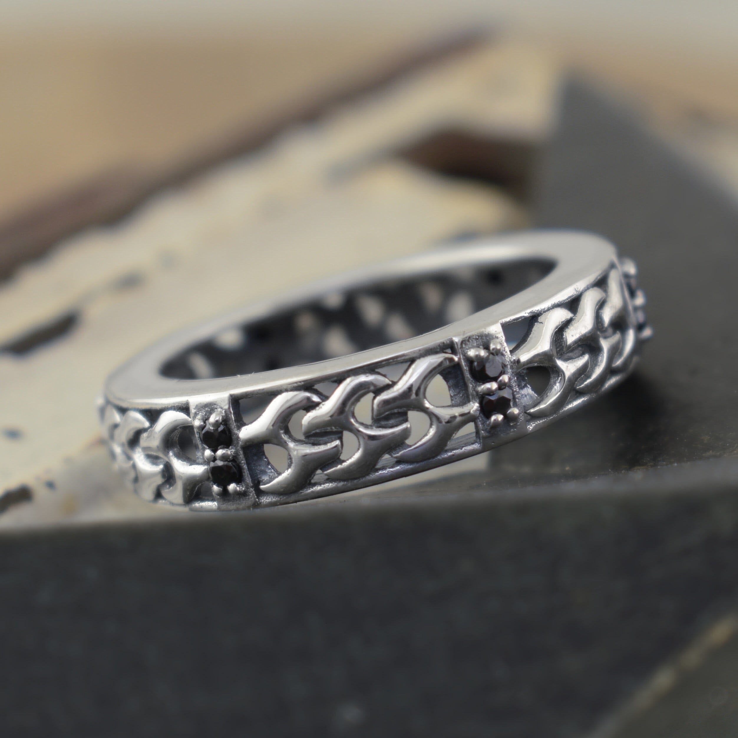A sterling silver high polish ring, with small faceted black gemstones and a chain-shaped band