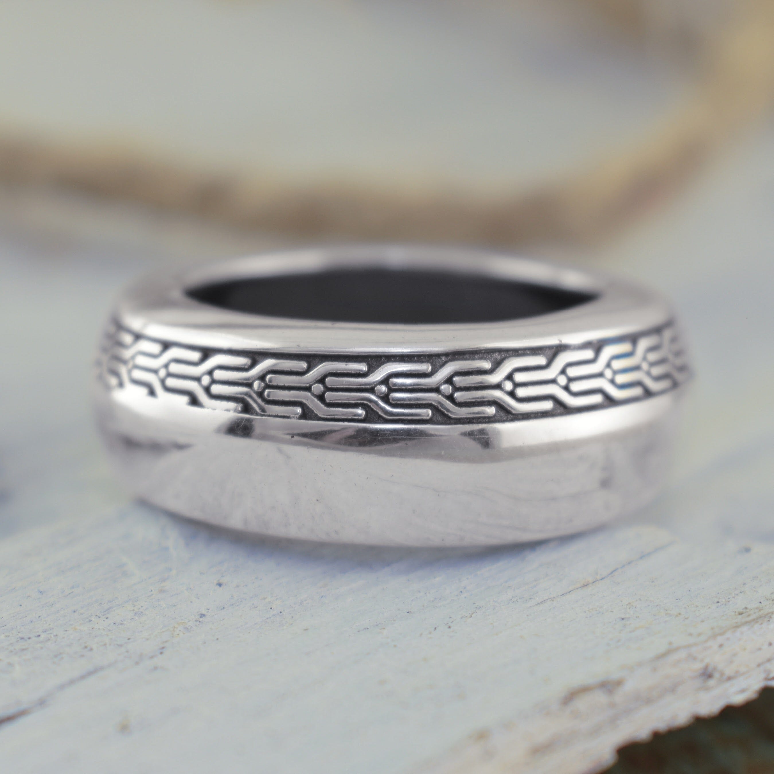 A polished sterling silver ring with a detailed geometric pattern along the band