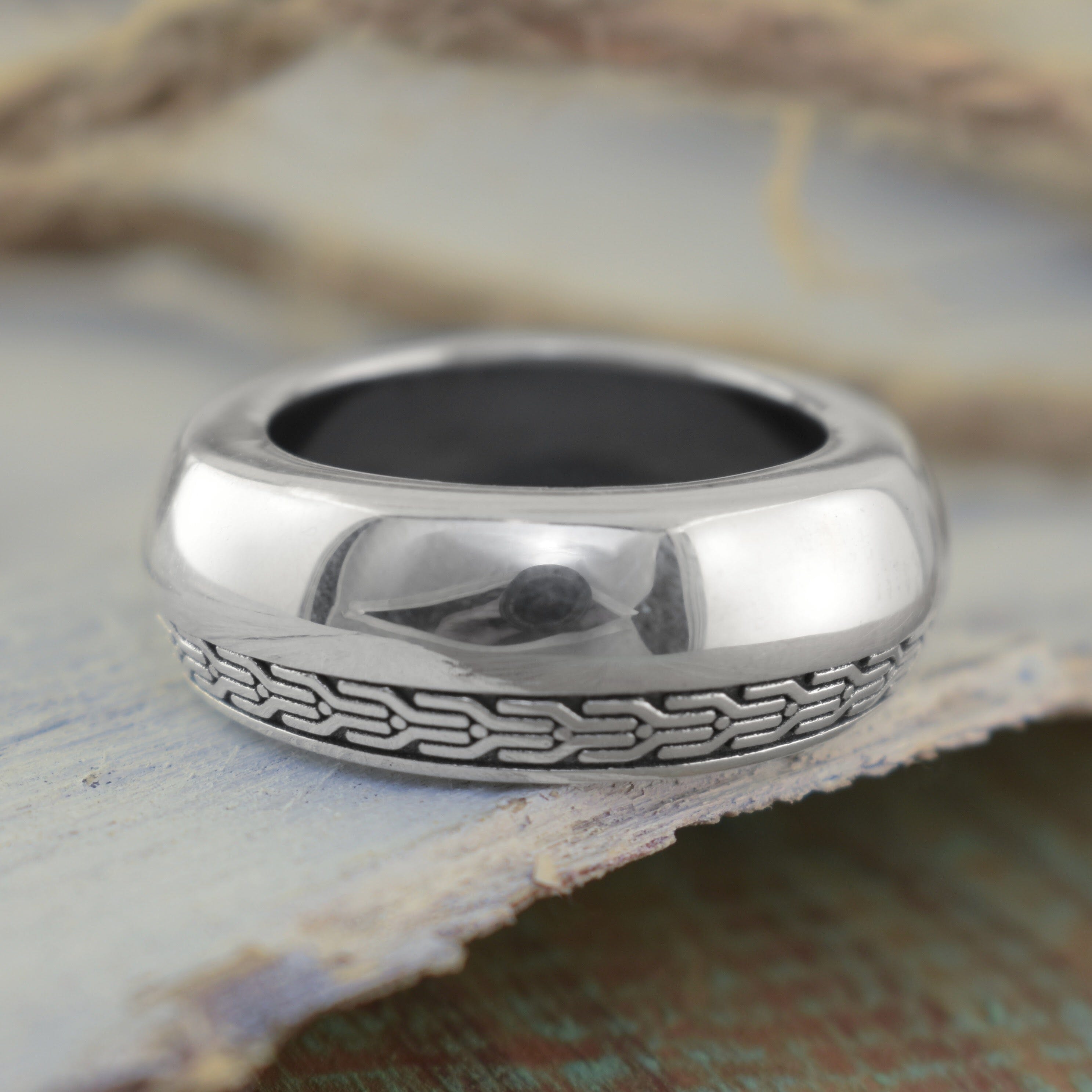 A polished sterling silver ring with a textured geometric pattern along the lower half