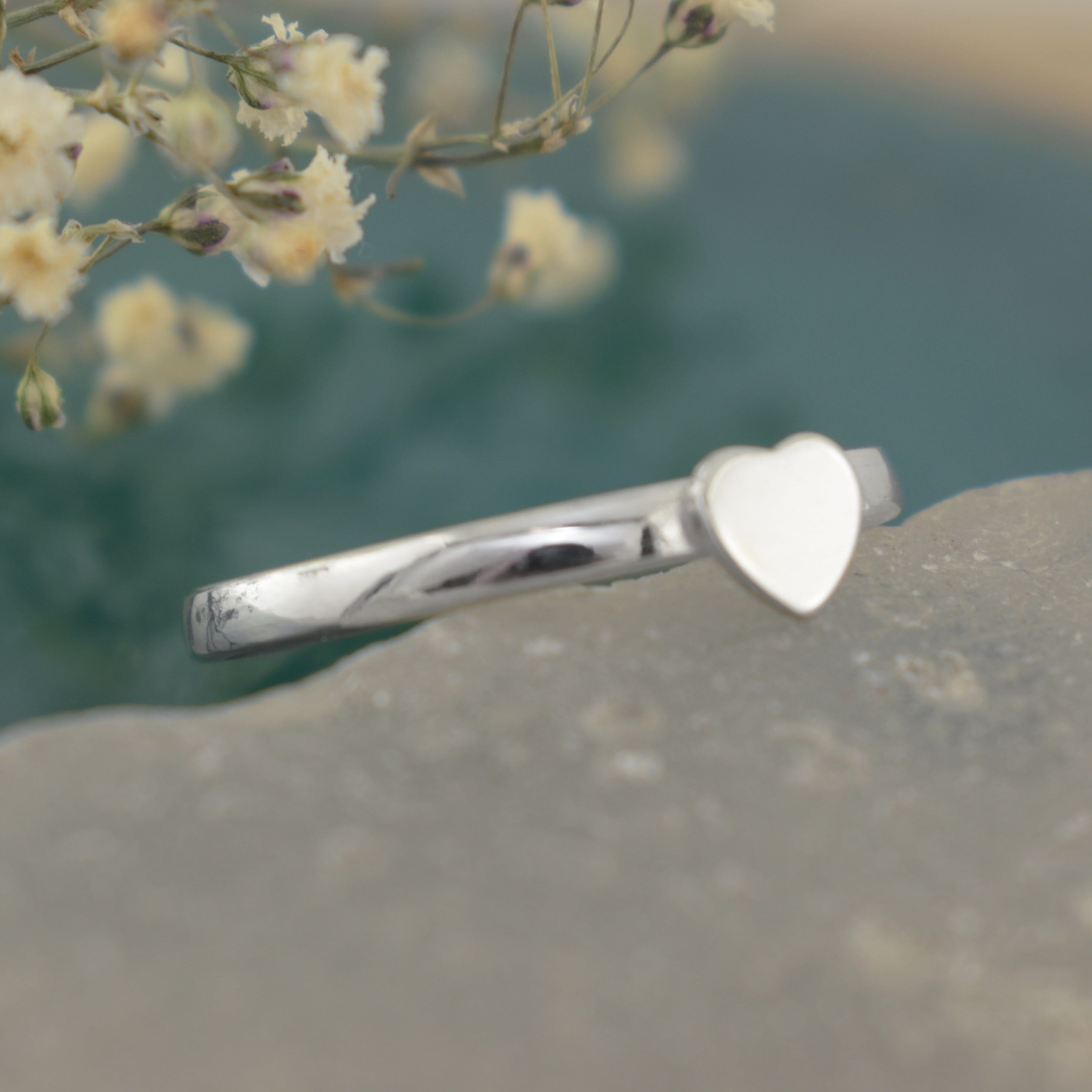A polished sterling silver ring with a small flat heart charm