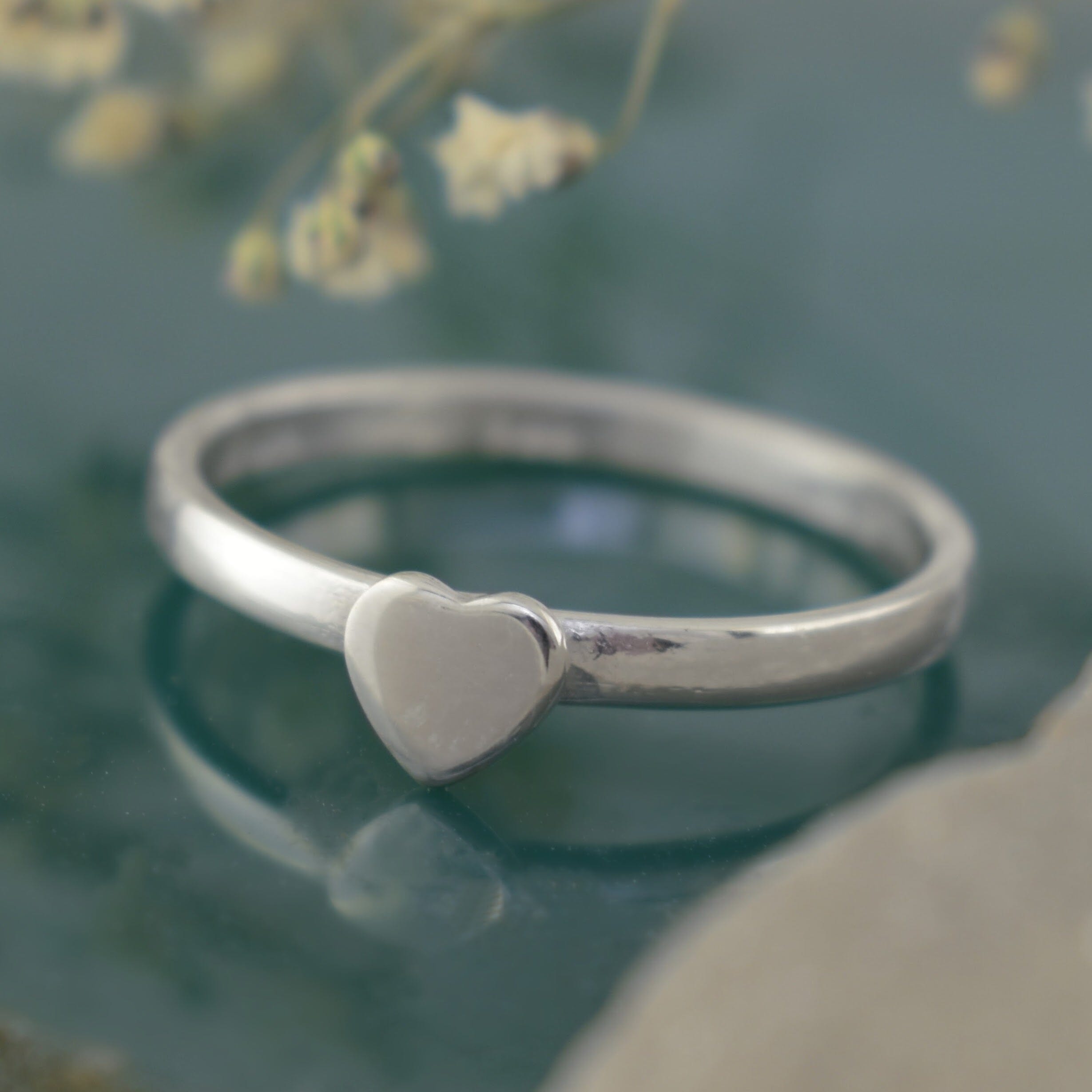 A polished sterling silver ring with a small heart-shaped charm