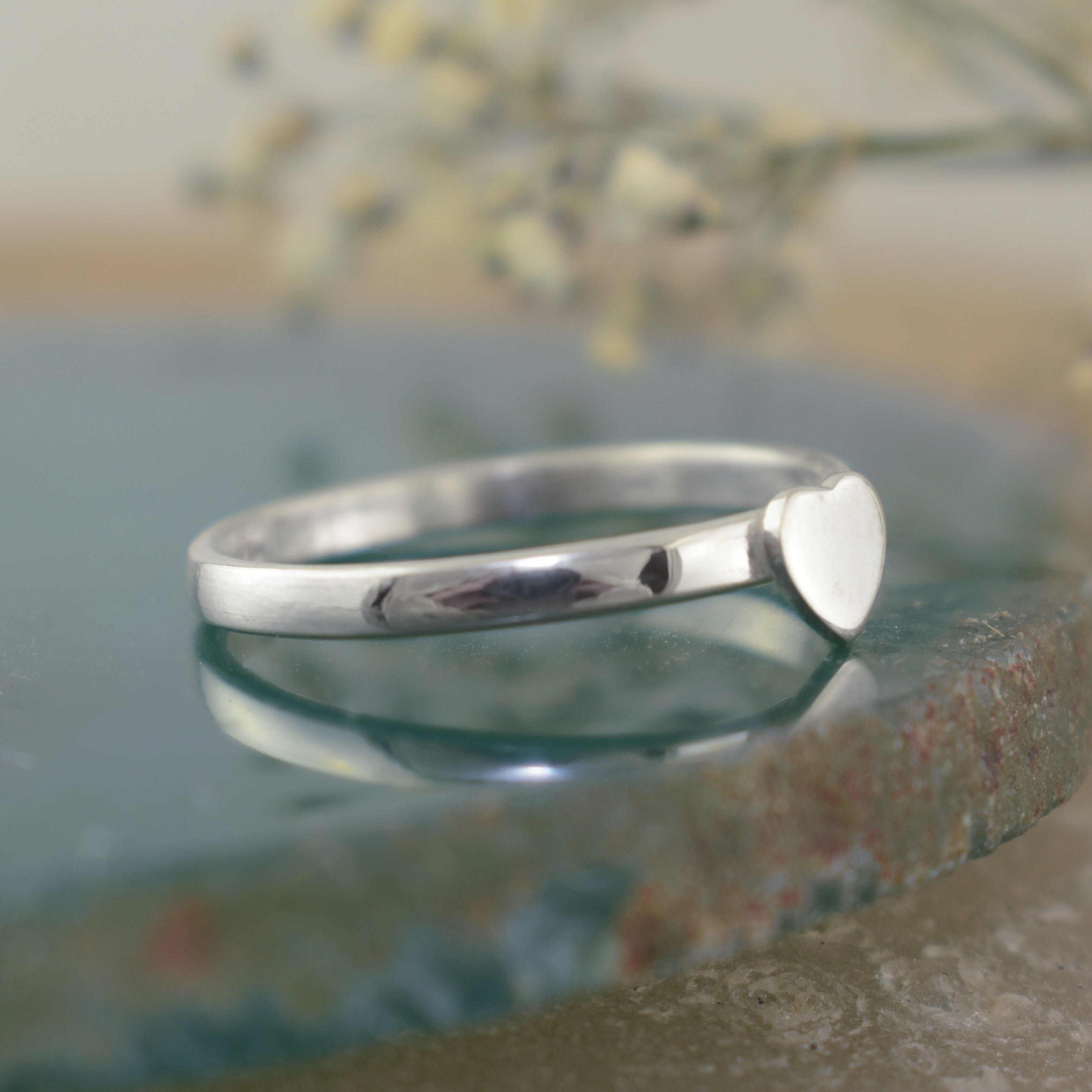 A minimalist sterling silver ring with a flat band and a small, polished heart-shaped charm
