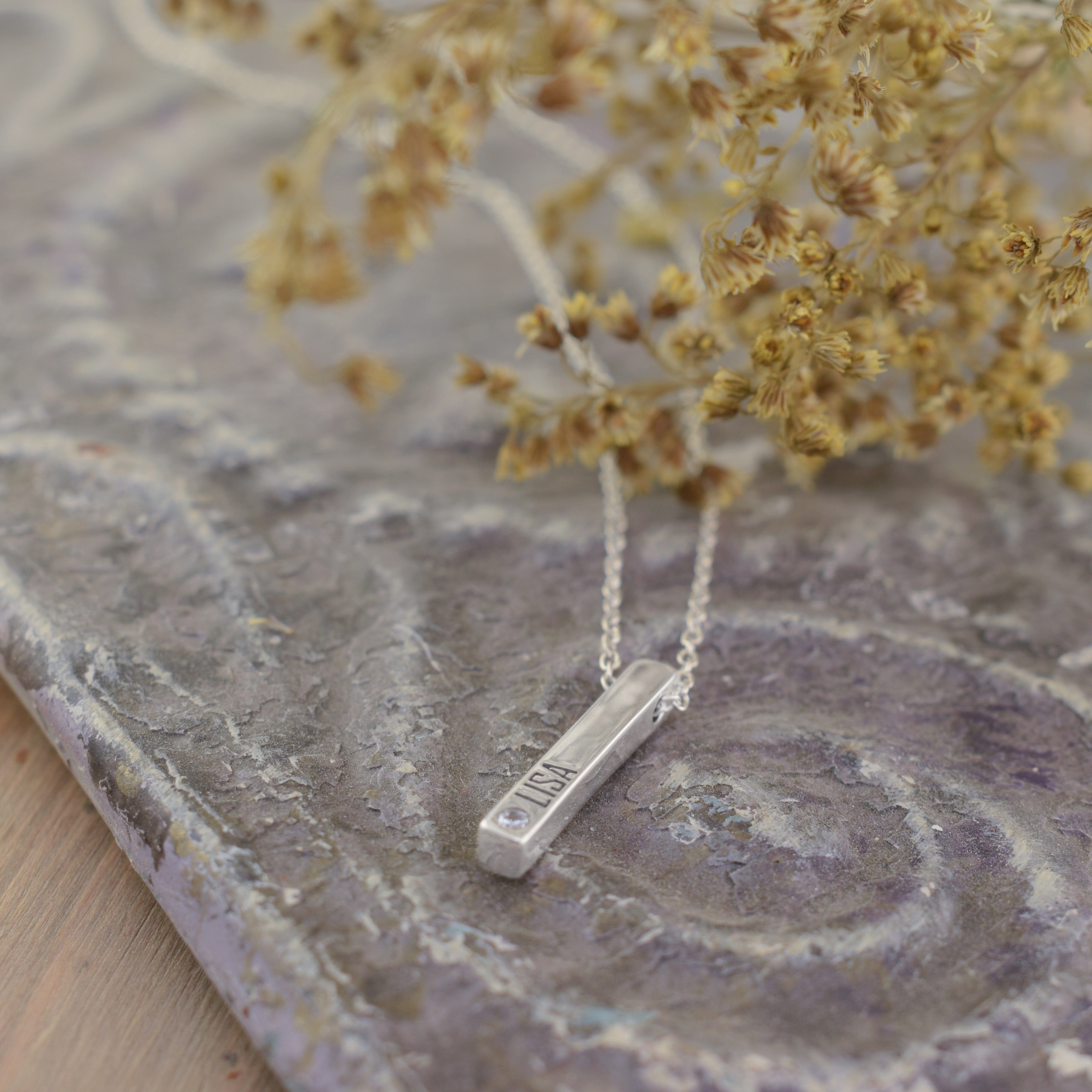 A sterling silver bar necklace engraved with 'LISA' and a small clear stone