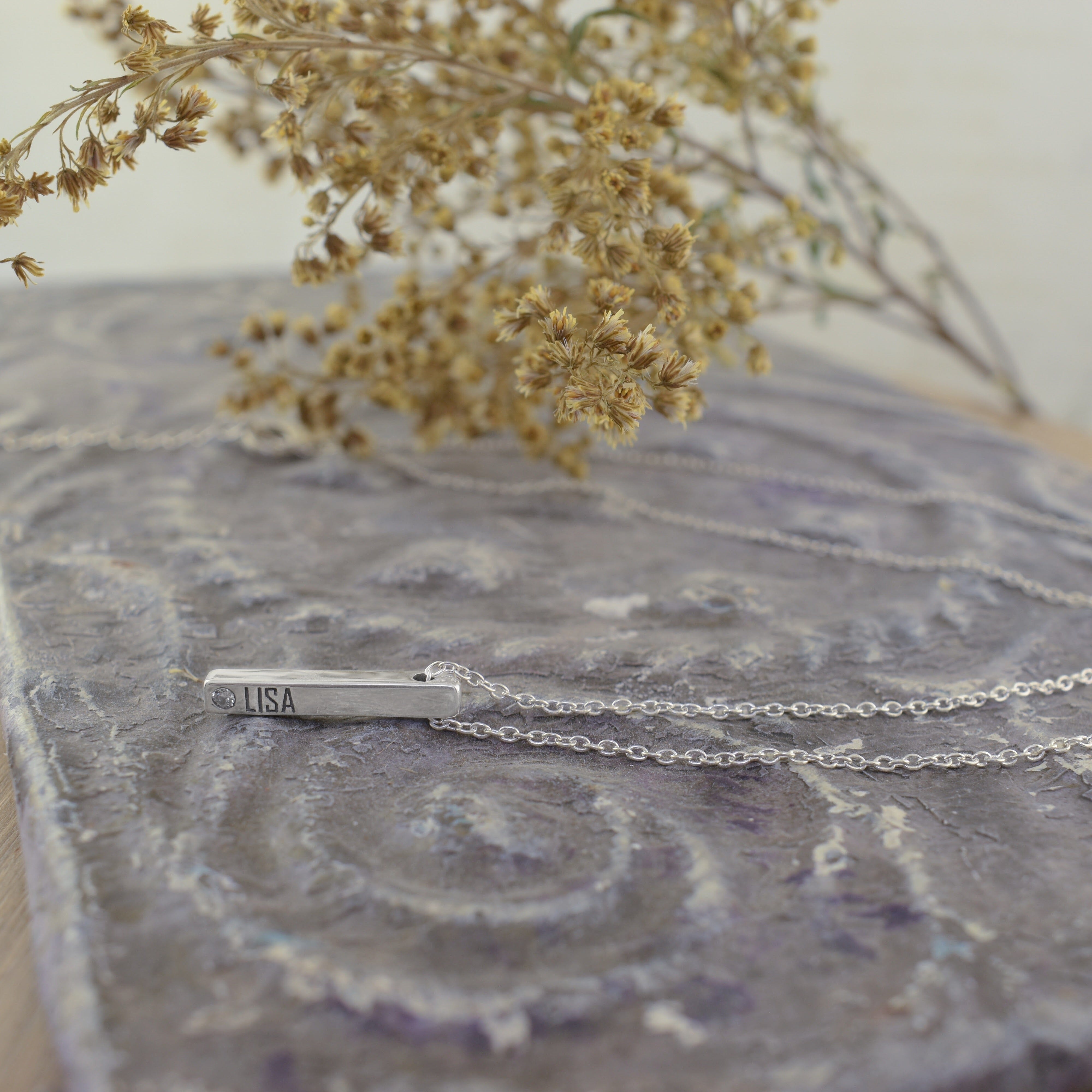 A sterling silver bar necklace engraved with 'LISA' and a small clear CZ gemstone