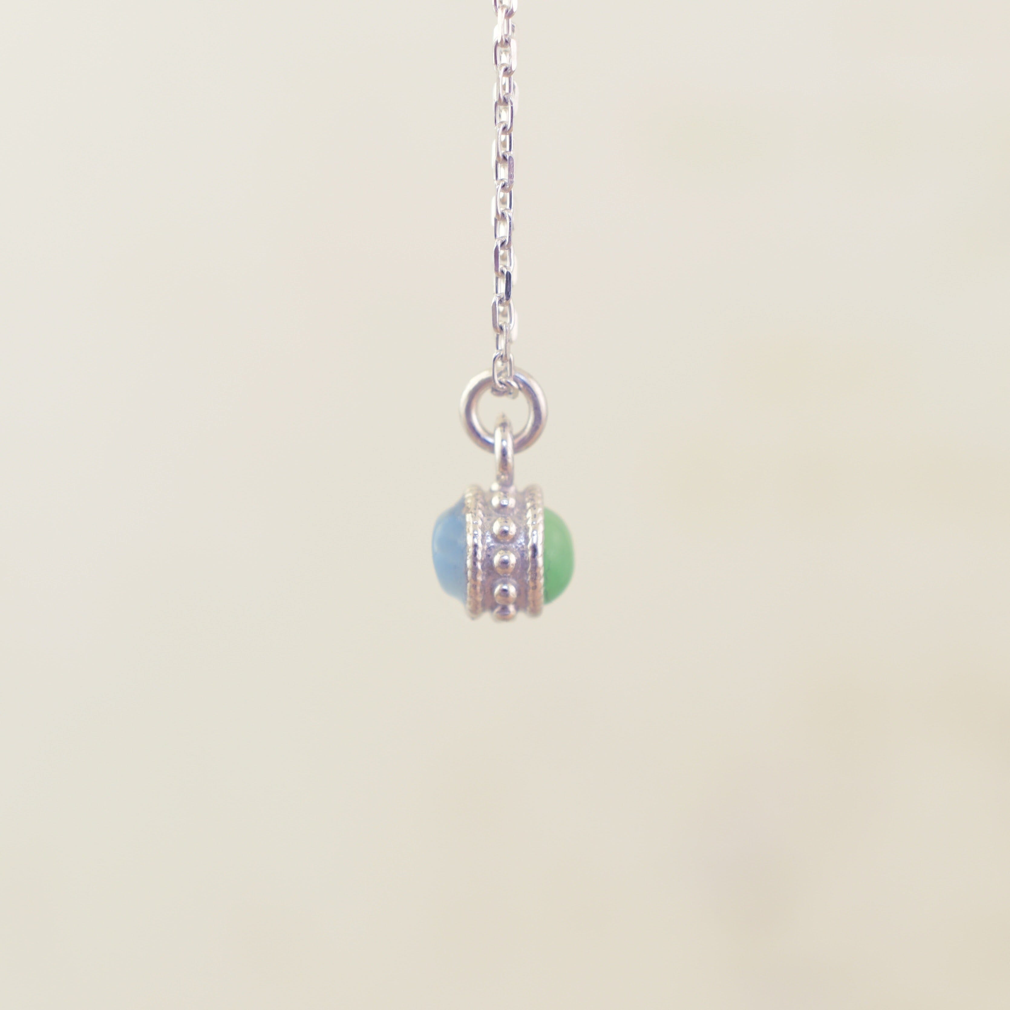 A sterling silver chain necklace with a small pendant featuring two round beads, one light blue and one light green