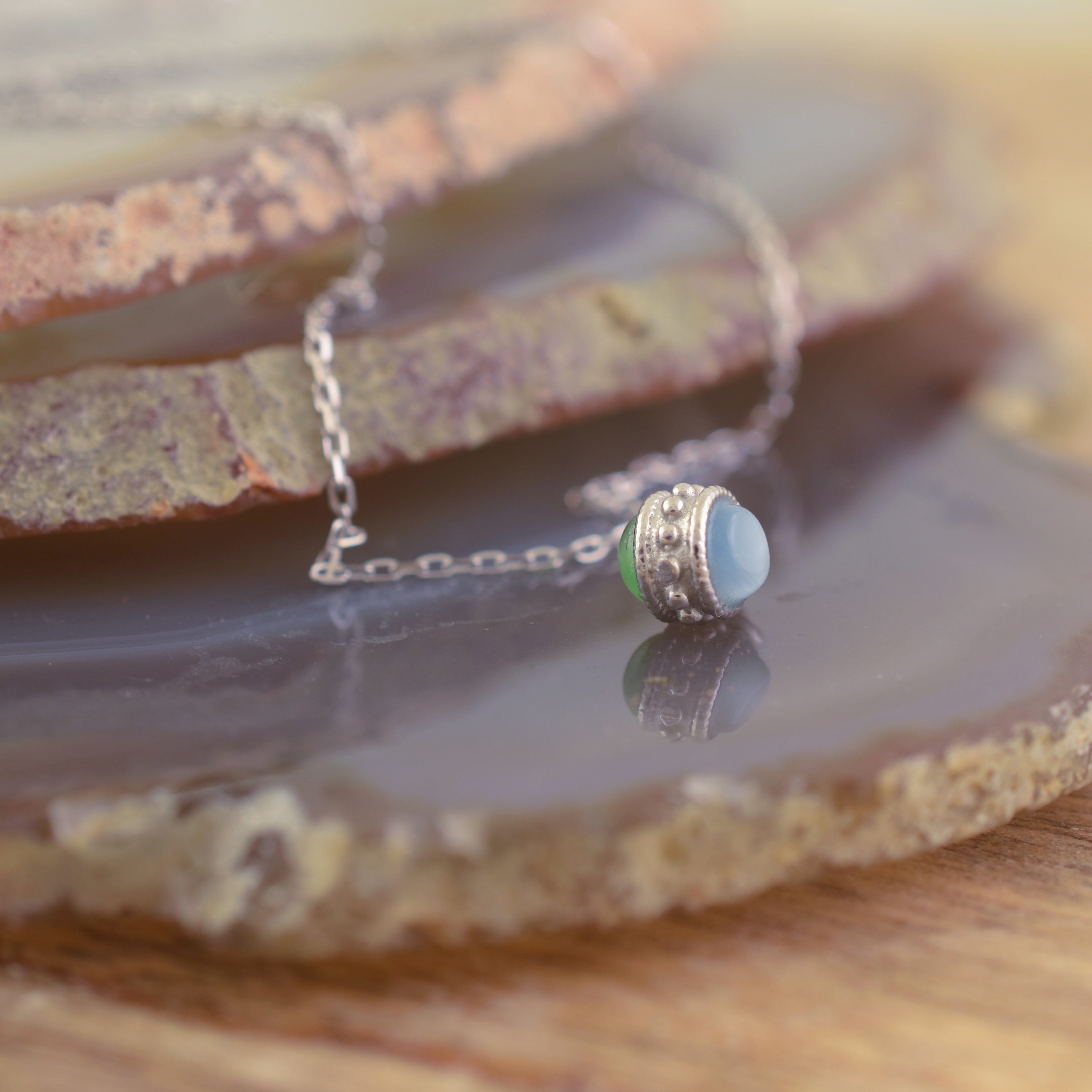 A sterling silver chain necklace with a small pendant featuring two round beads, one light blue and one light green