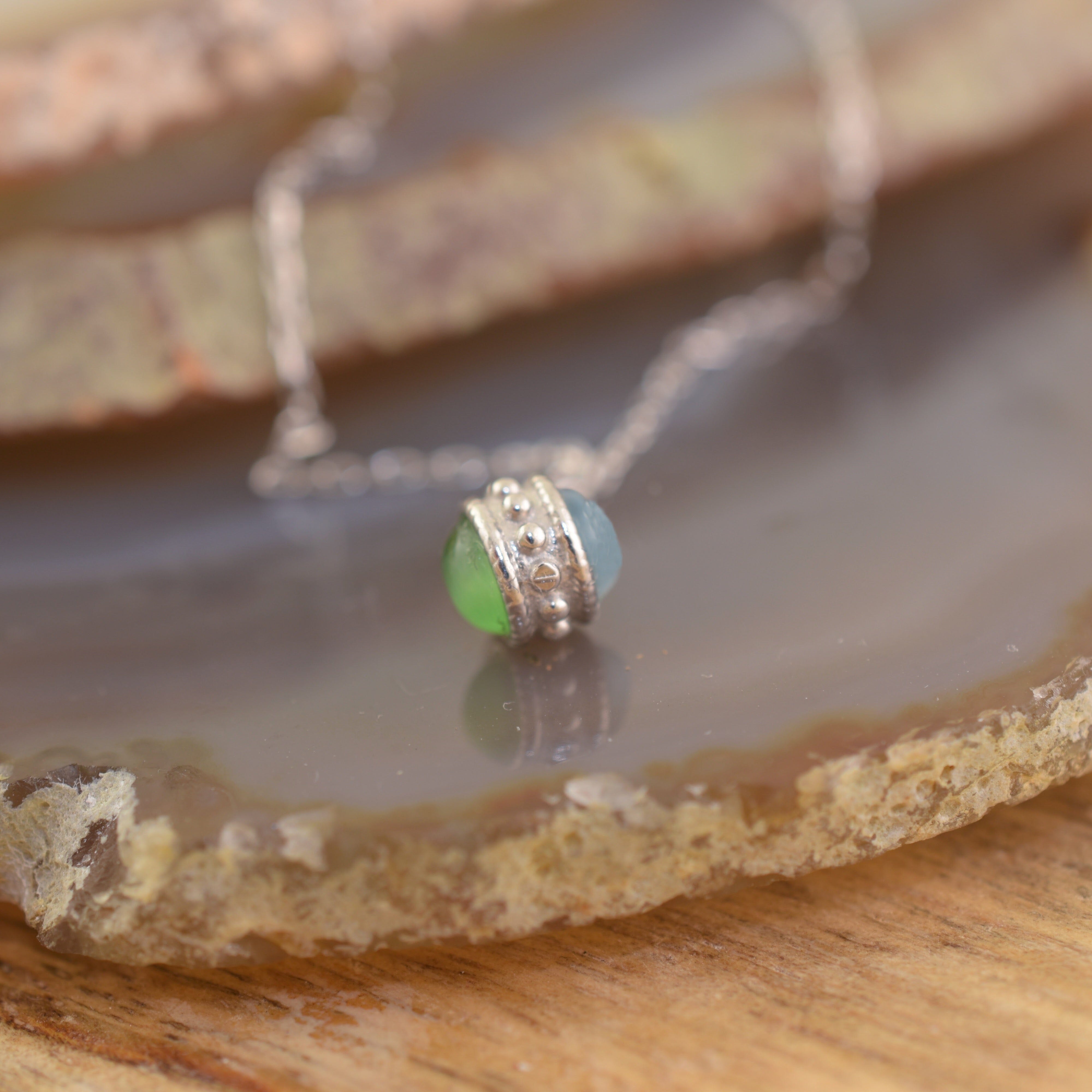 A sterling silver chain necklace with a small pendant featuring two round beads, one light blue and one light green