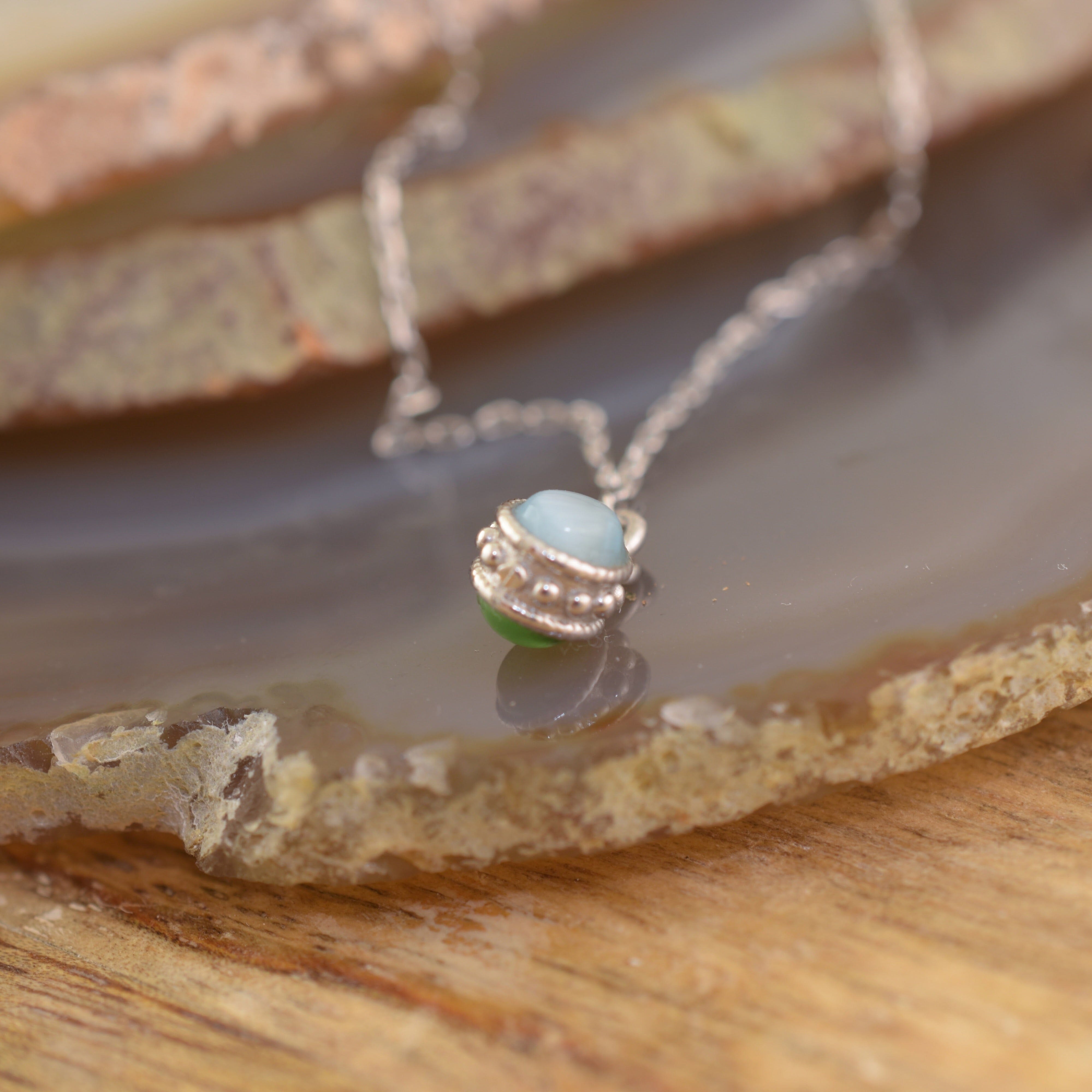 A sterling silver chain necklace with a small pendant featuring two round beads, one light blue and one light green