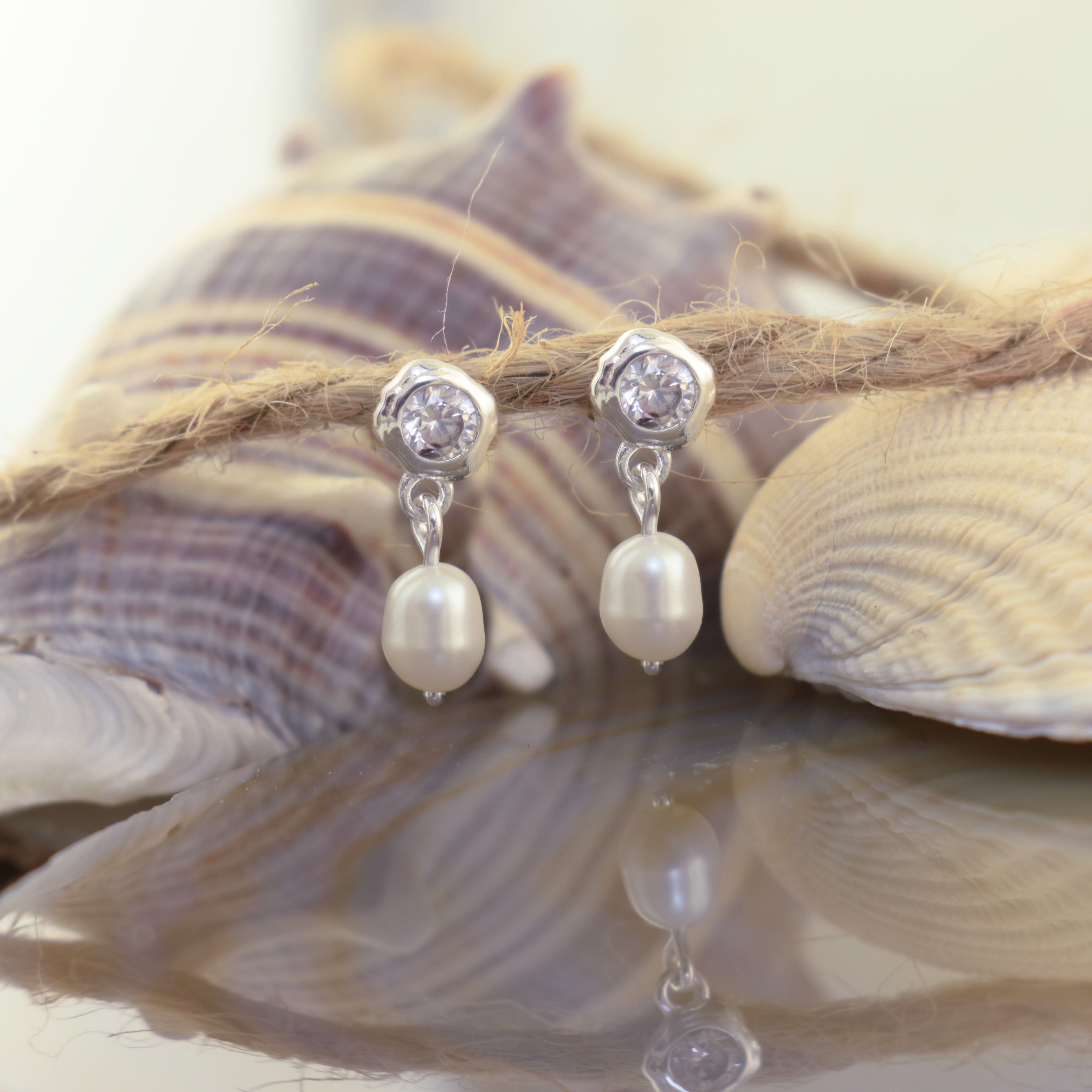 A pair of Zamak dangle earrings with clear round stones at the top and white pearl drops below