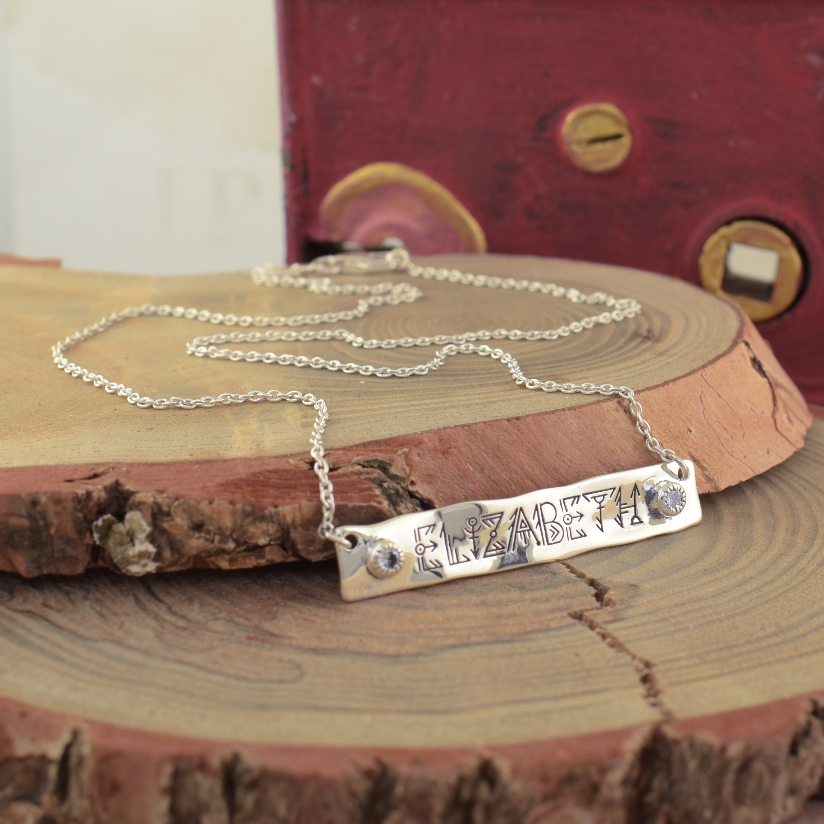 A sterling silver bar necklace with the name 'ELIZABETH' hand-stamped on the bar and small clear stones on the ends