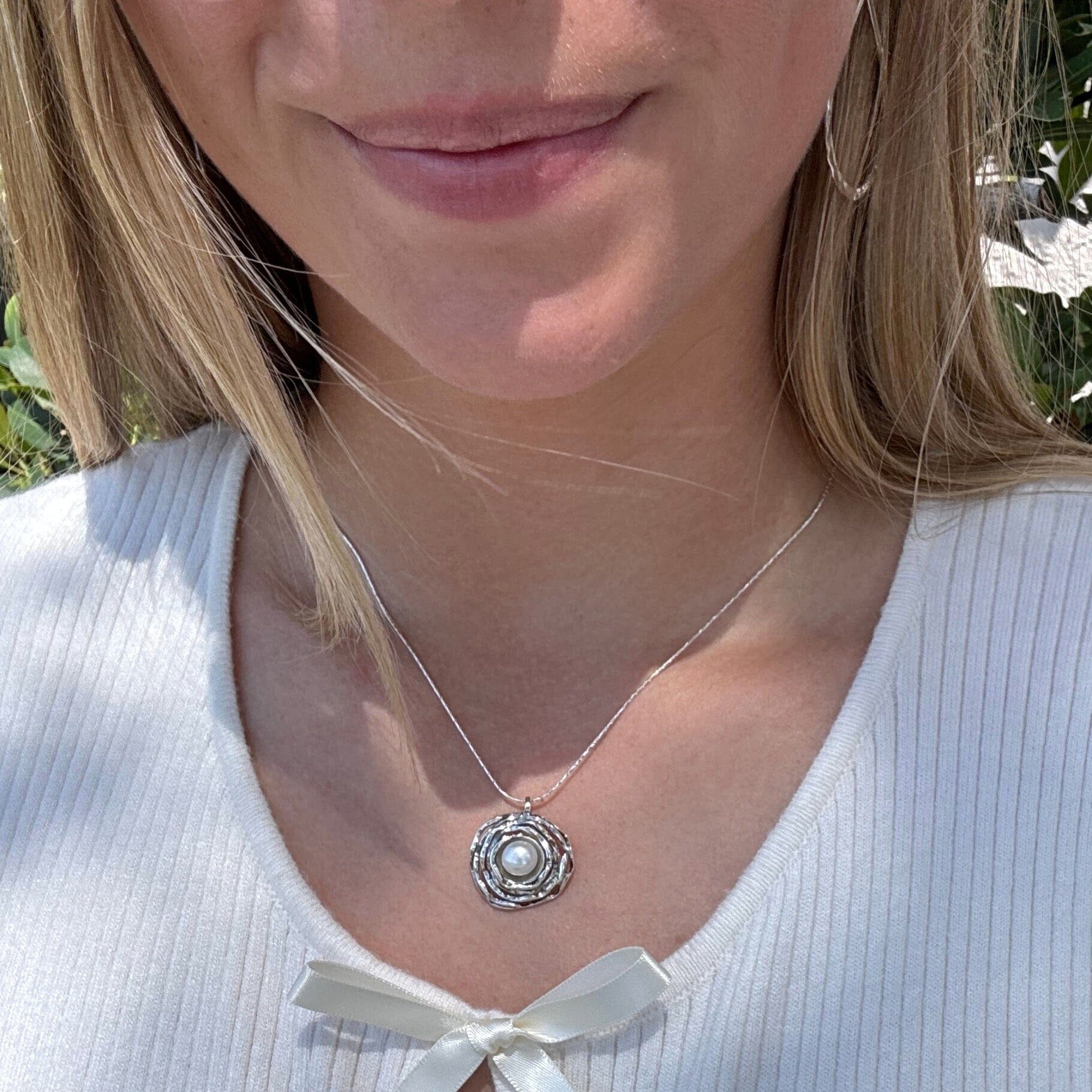 chunky, circular silver pendant with a freshwater pearl center on a silver chain