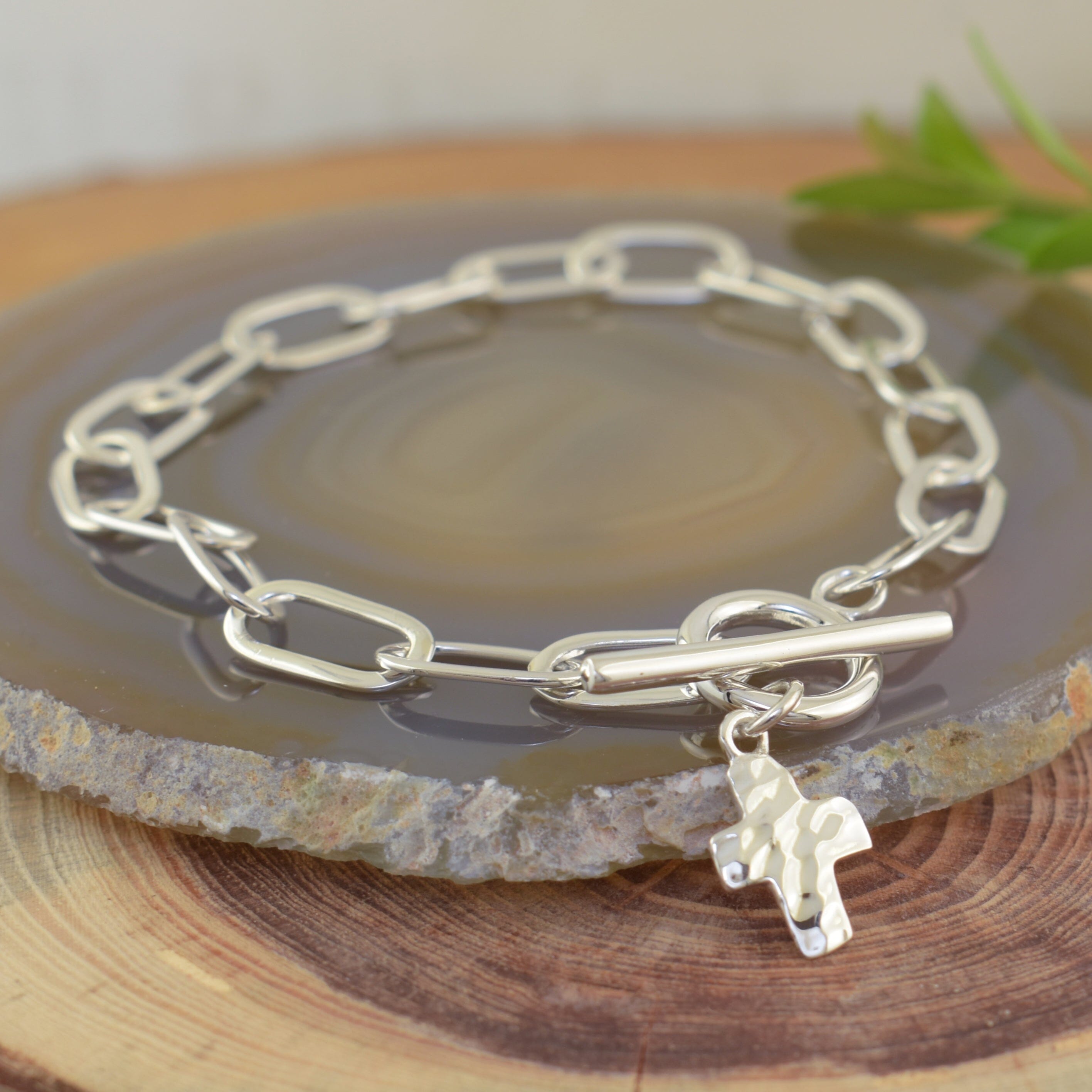 a sterling silver bracelet with a linked chain and a hammered cross pendant hanging from the closure