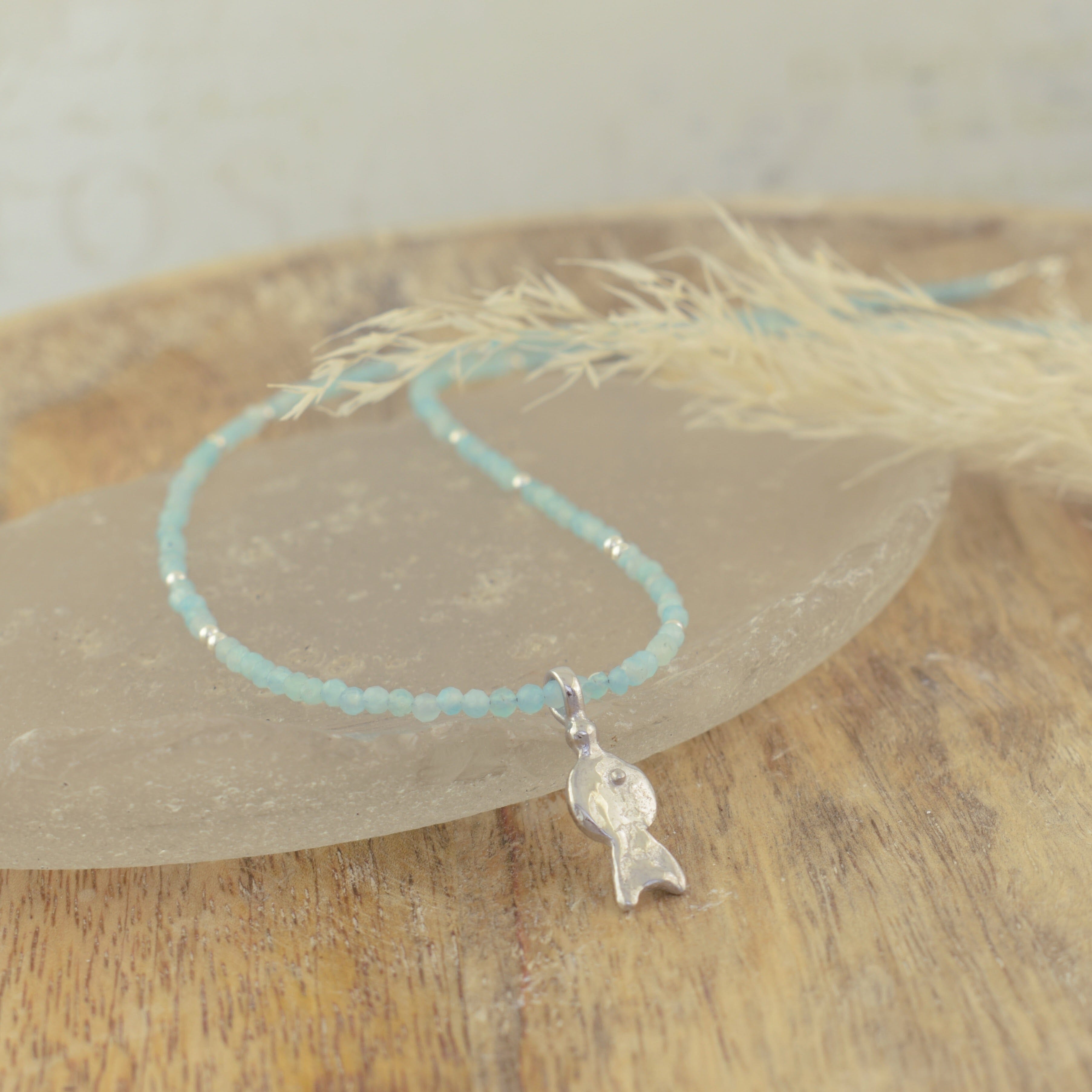 A handcrafted necklace with light blue faceted beads and a small silver fish pendant