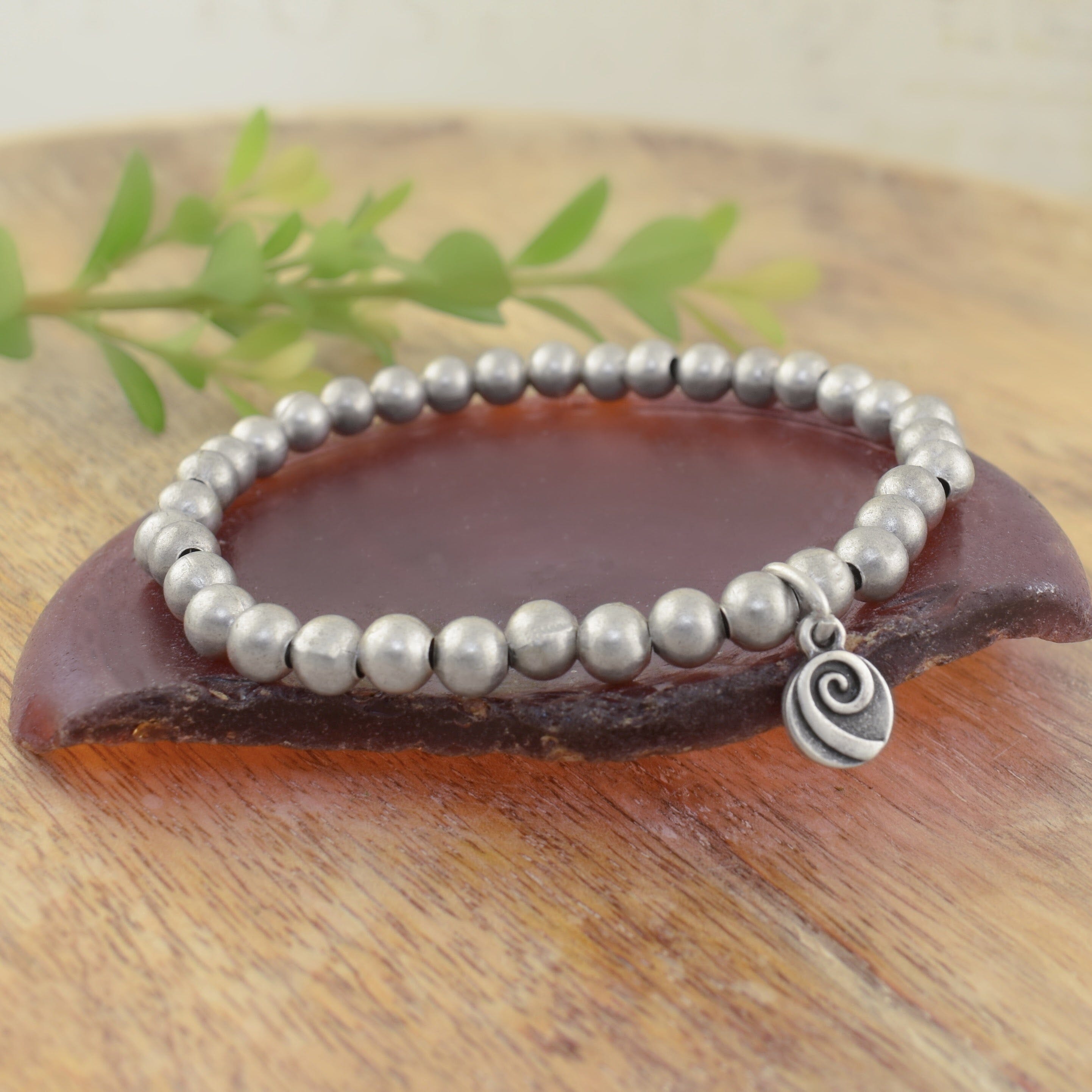 A beaded stretch bracelet made of matte silver round beads with a small logo charm