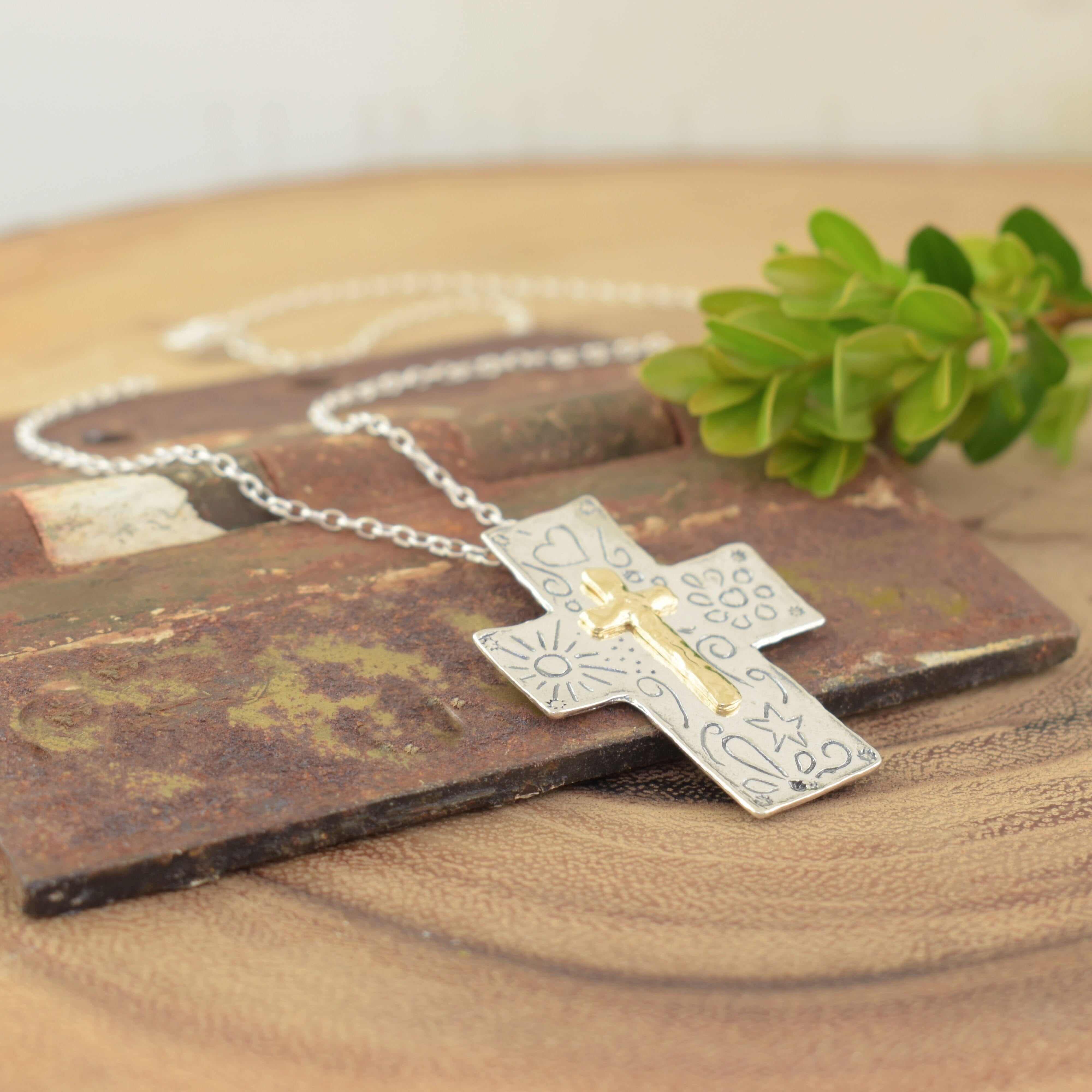 hand-etched sterling silver cross decorated with symbols like the sun, heart, bloom, and star.