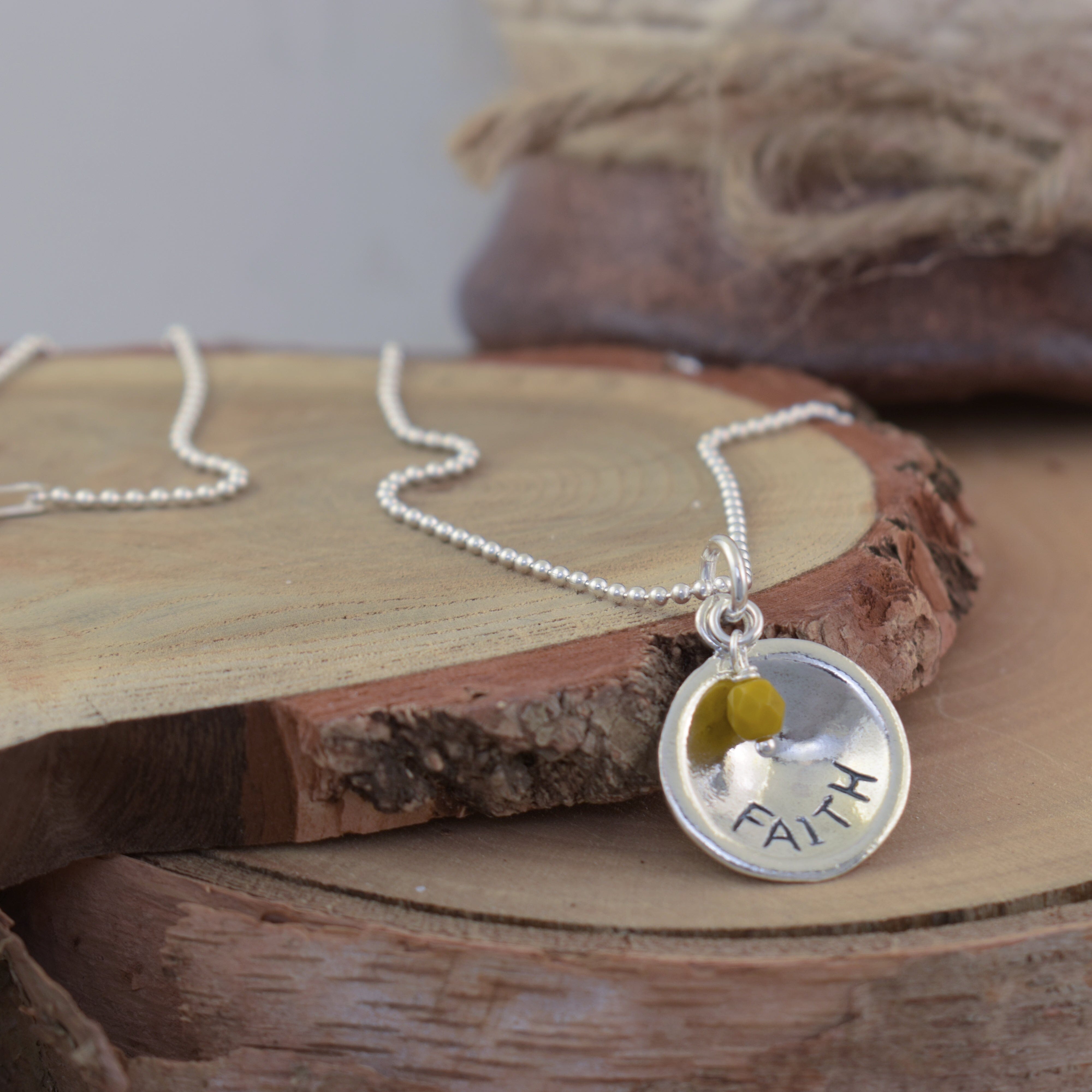 delicate necklace featuring a yellow bead and a silver concave pendant stamped with the word Faith