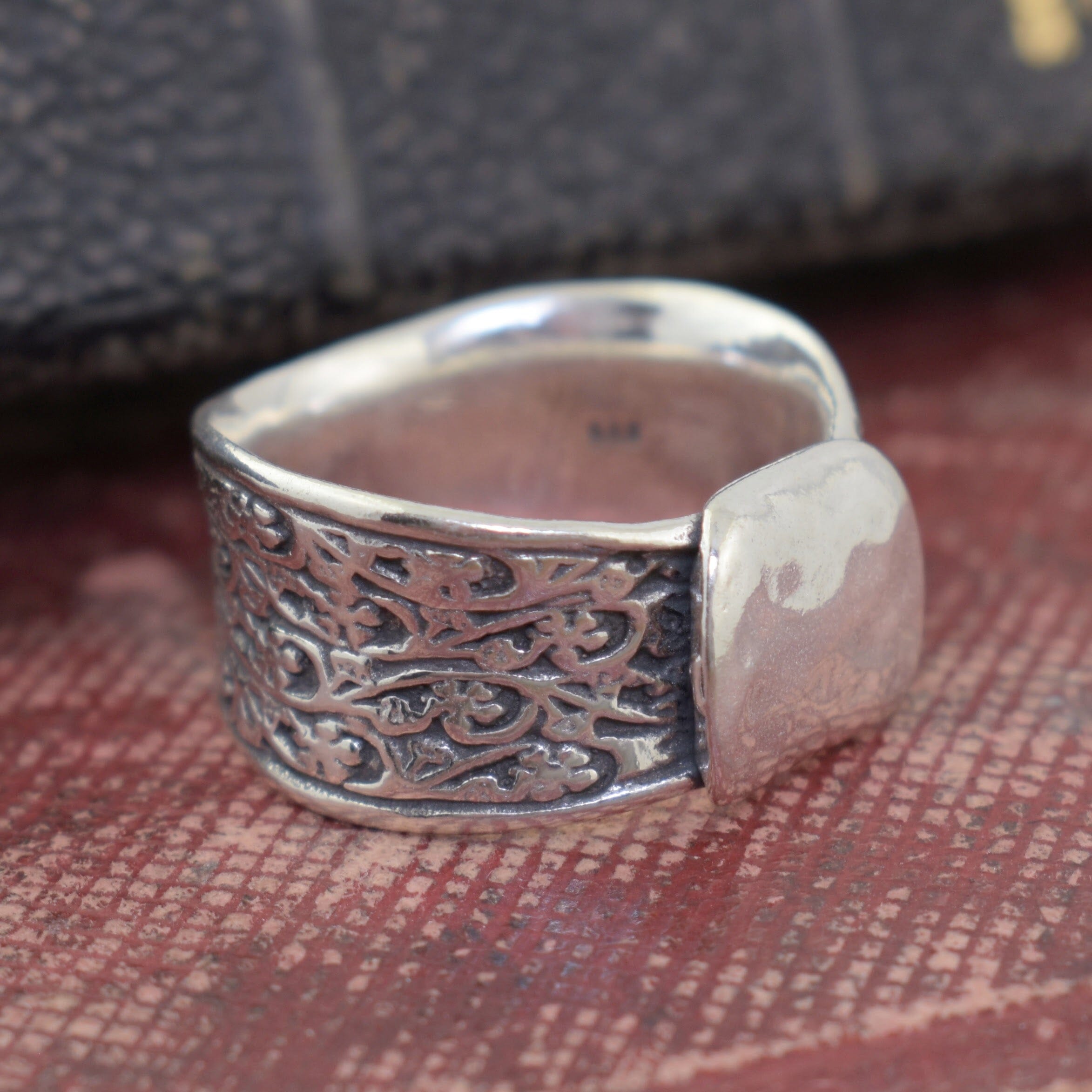 Silver ring with intricate designs on a textured surface