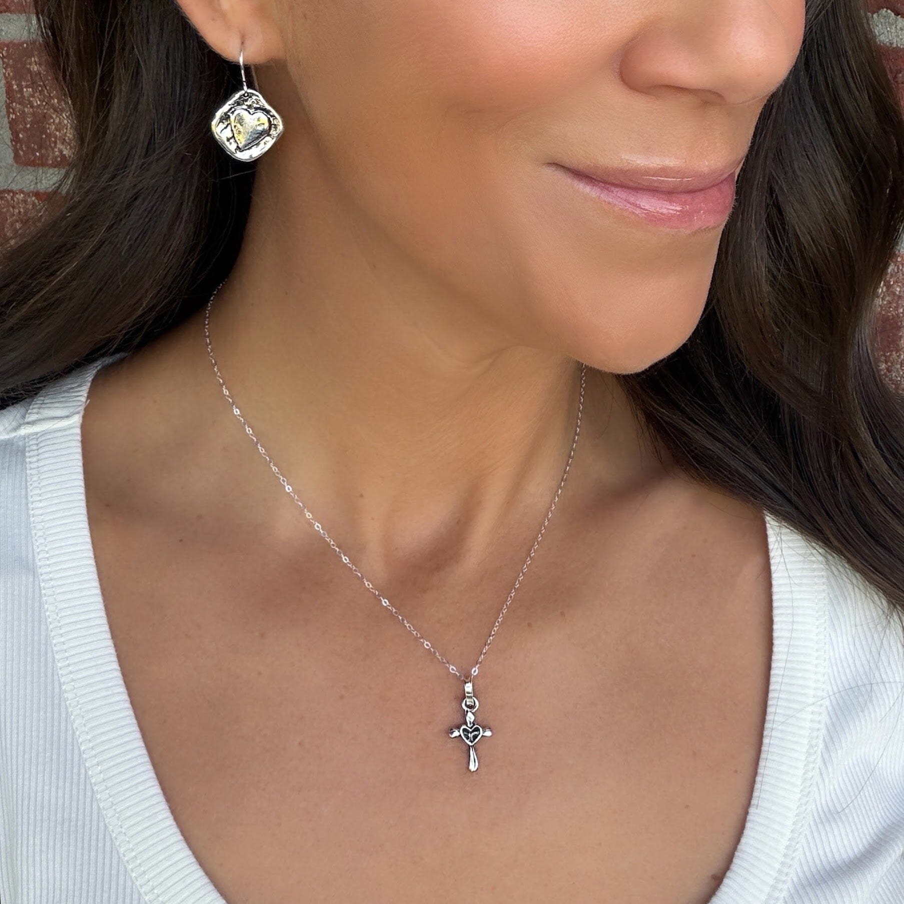 silver cross pendant with a heart center suspended from a delicate rolo style chain