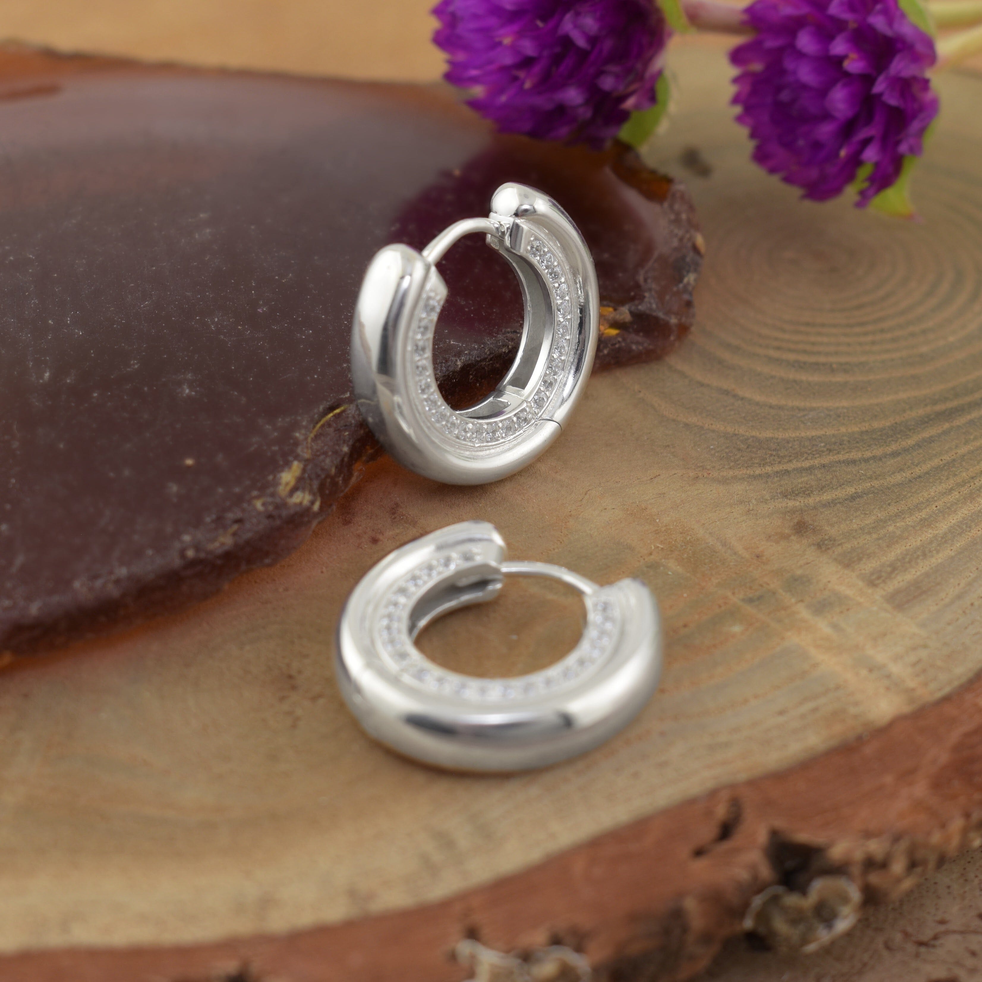 a pair of polished silver hoop earrings with small clear stones along the front curve