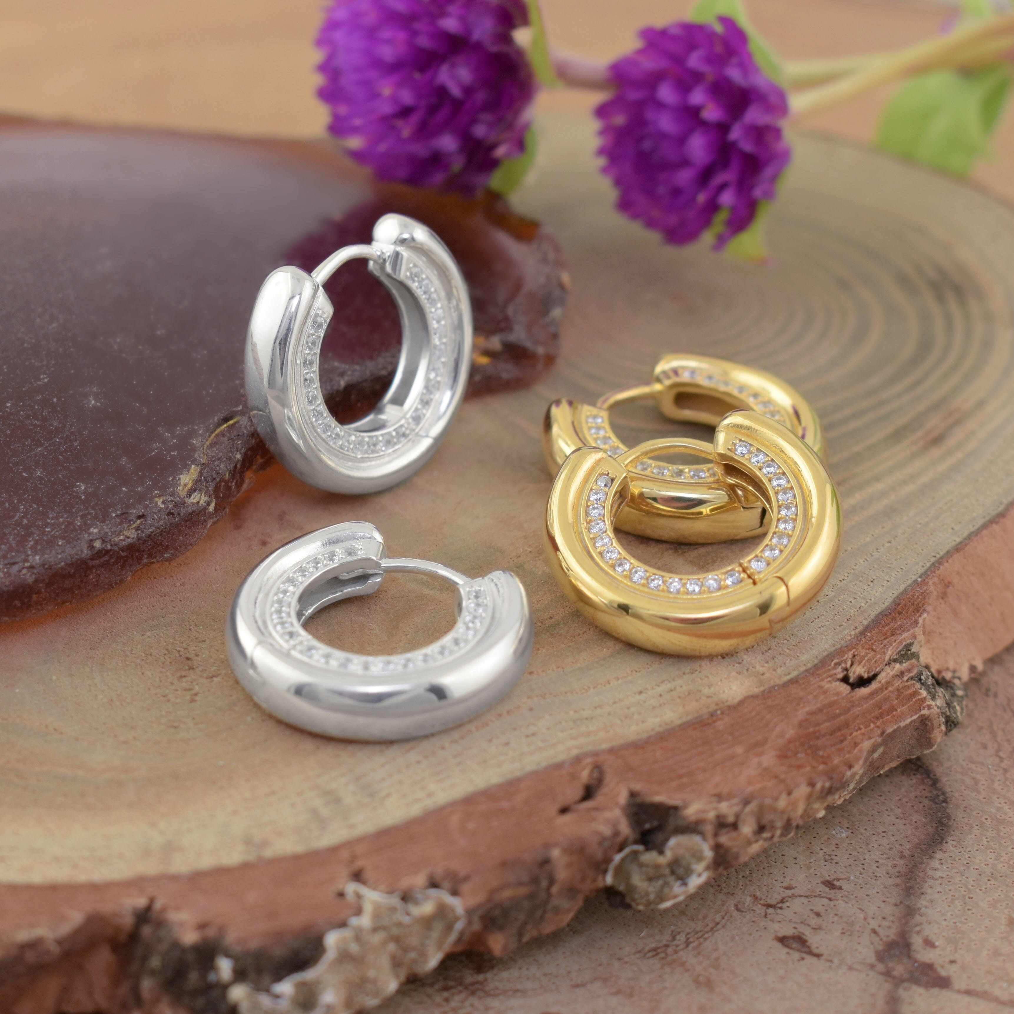 two pairs of small hoop earrings, one in polished silver, one in polished gold, each set with clear stones
