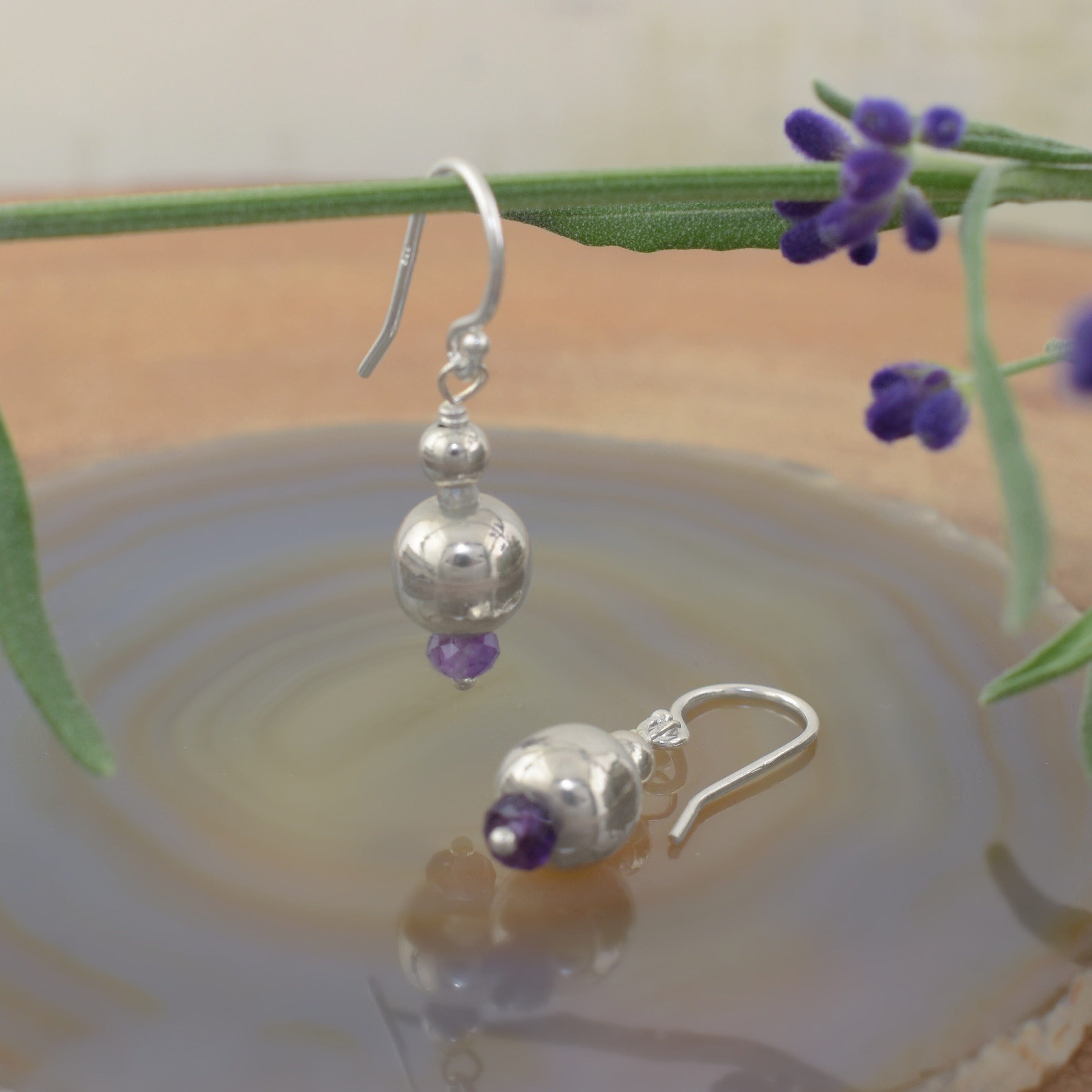 A pair of dangly sterling silver ball earrings with a small amethyst stone on the end