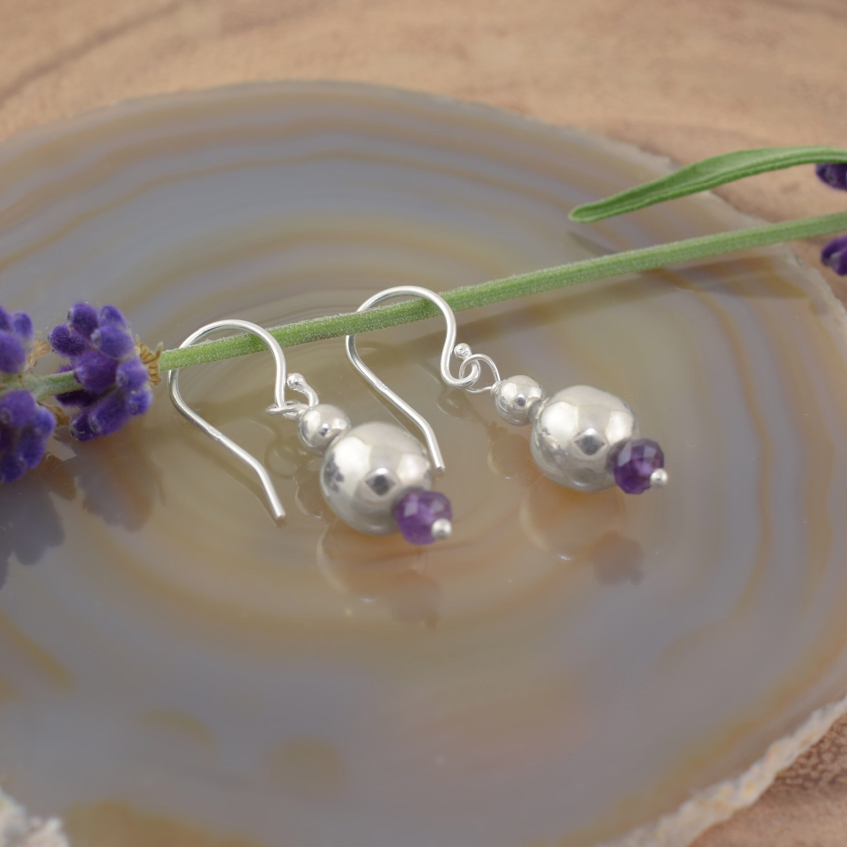A pair of dangly sterling silver ball earrings with a small amethyst stone on the end