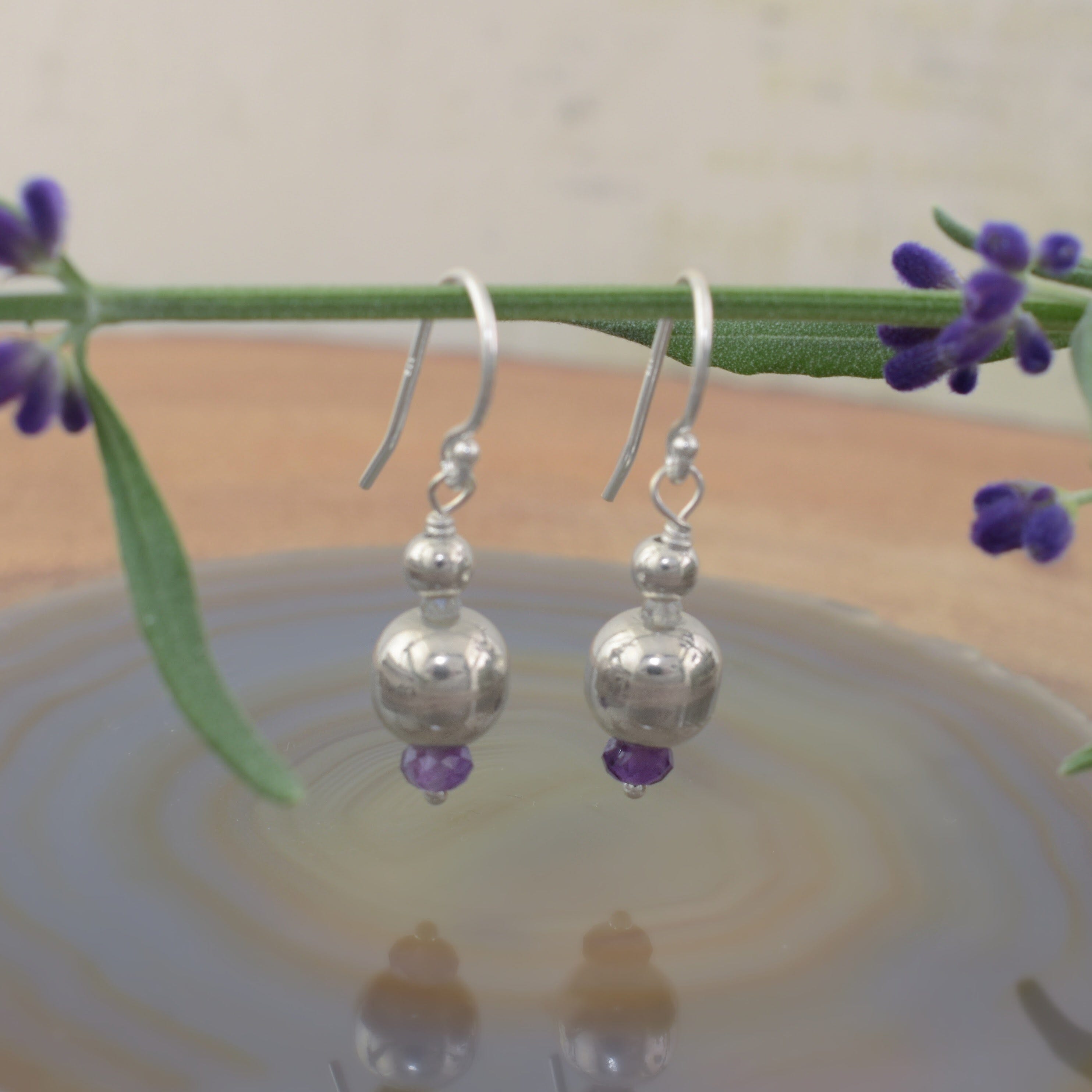 A pair of dangly sterling silver ball earrings with a small amethyst stone on the end