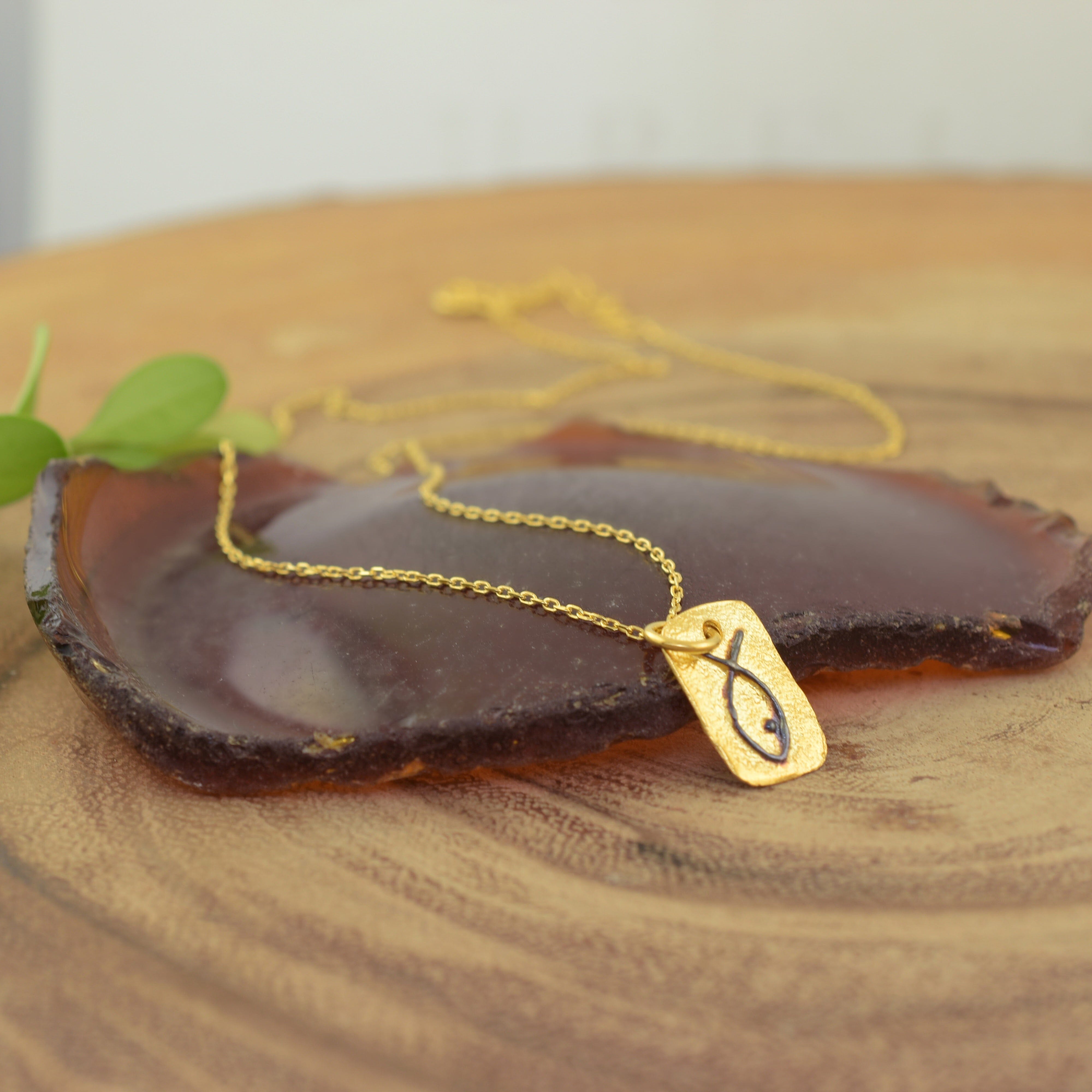 A gold necklace with a rectangular pendant, featuring a fish-shaped outline