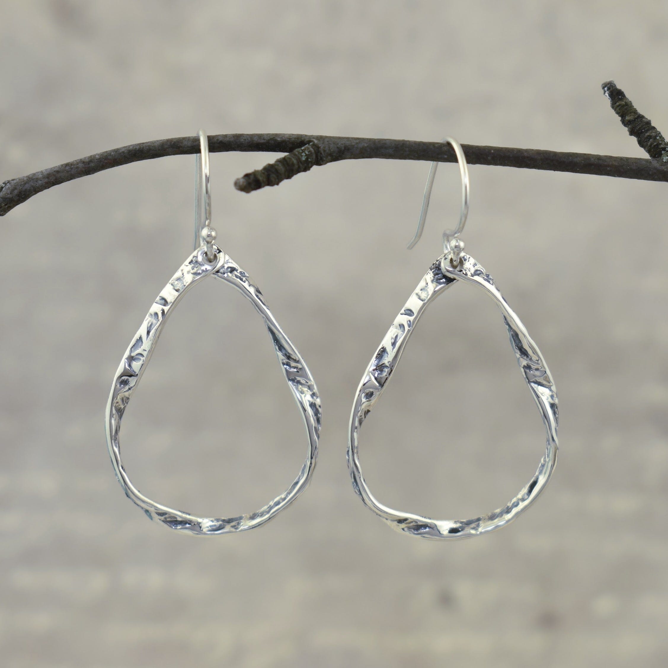 A pair of sterling silver teardrop-shaped dangle earrings with a textured, hammered finish