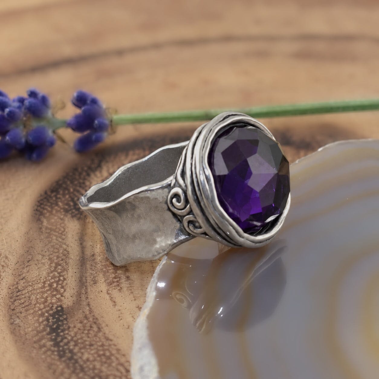 A sterling silver ring with an organic wide band, featuring a large round synthetic amethyst stone in the center