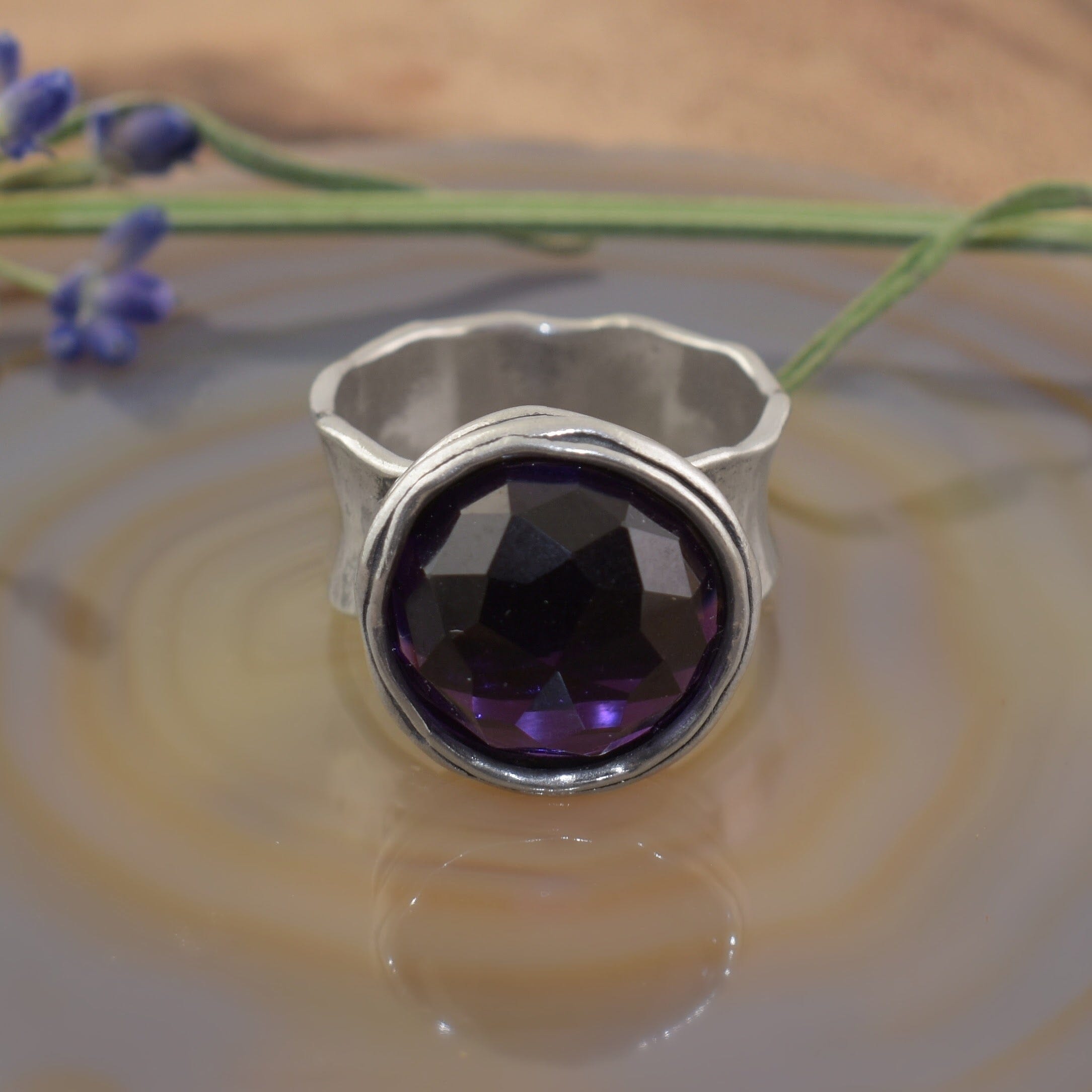 A sterling silver ring with an organic wide band, featuring a large round synthetic amethyst stone in the center