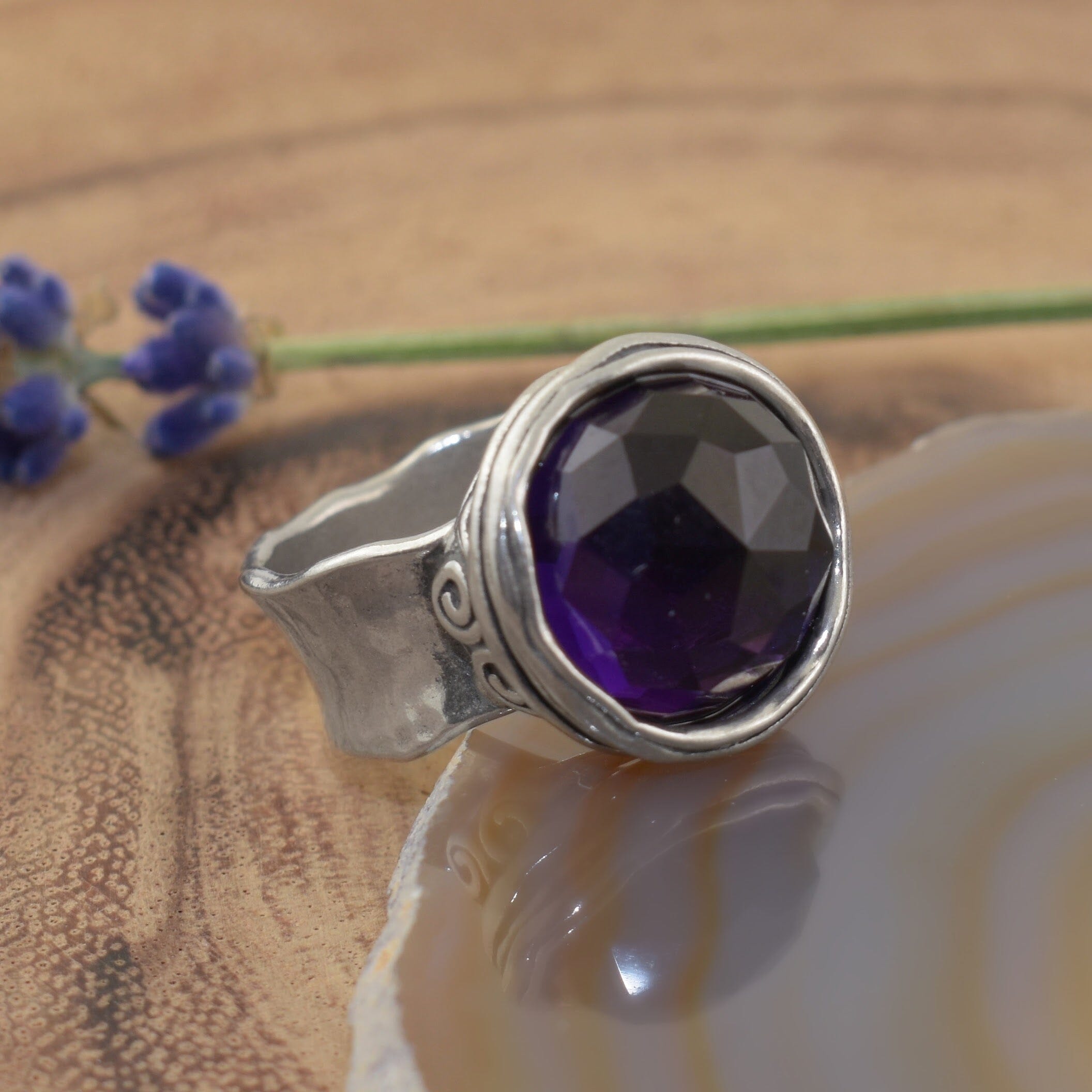 A sterling silver ring with an organic wide band, featuring a large round synthetic amethyst stone in the center
