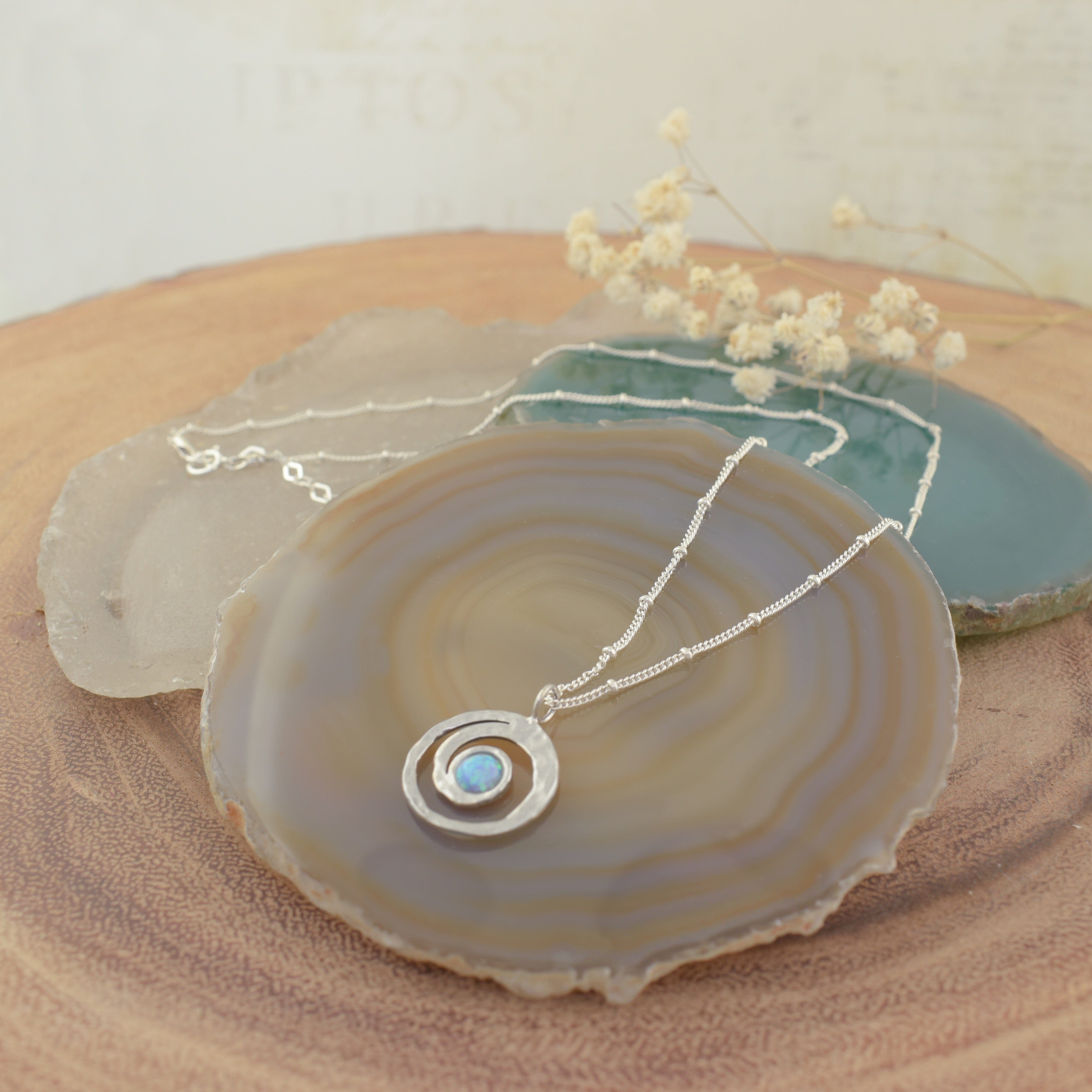 A sterling silver necklace with small silver beads spaced along the chain, featuring a round spiral pendant with an opal stone resting in the middle