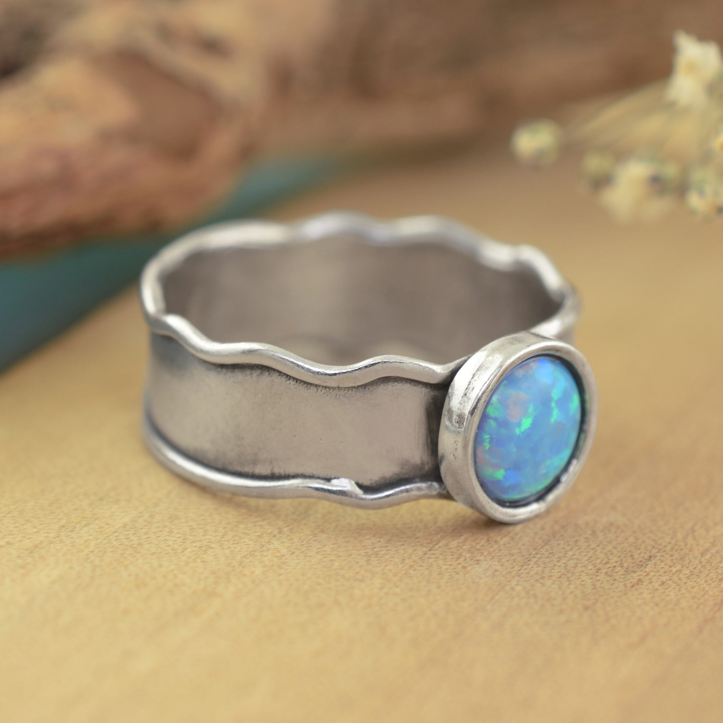 A sterling silver ring with a wavy, hammered texture and a round bezel-set blue opal stone