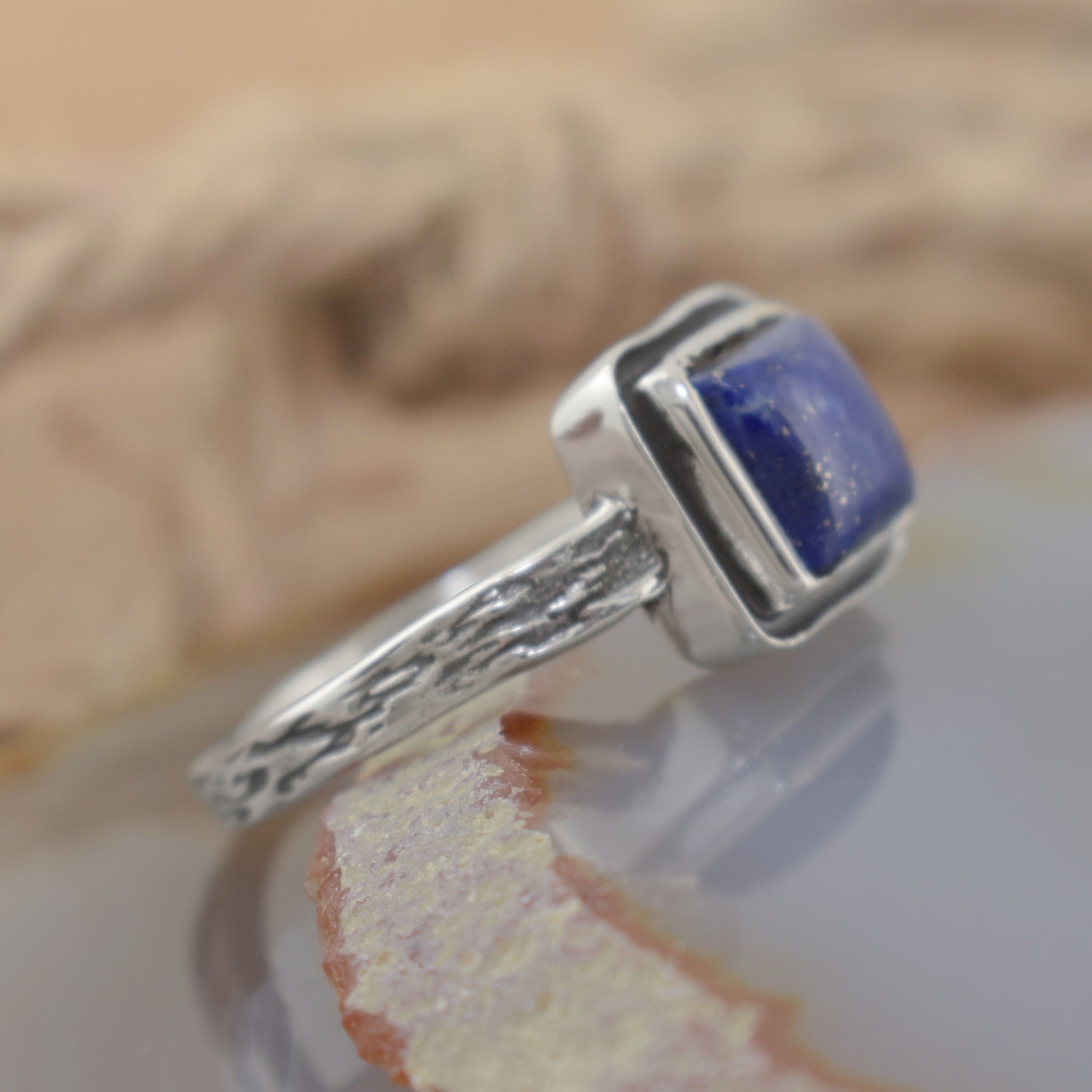 A sterling silver ring with a textured band, featuring a square dark blue stone in the middle