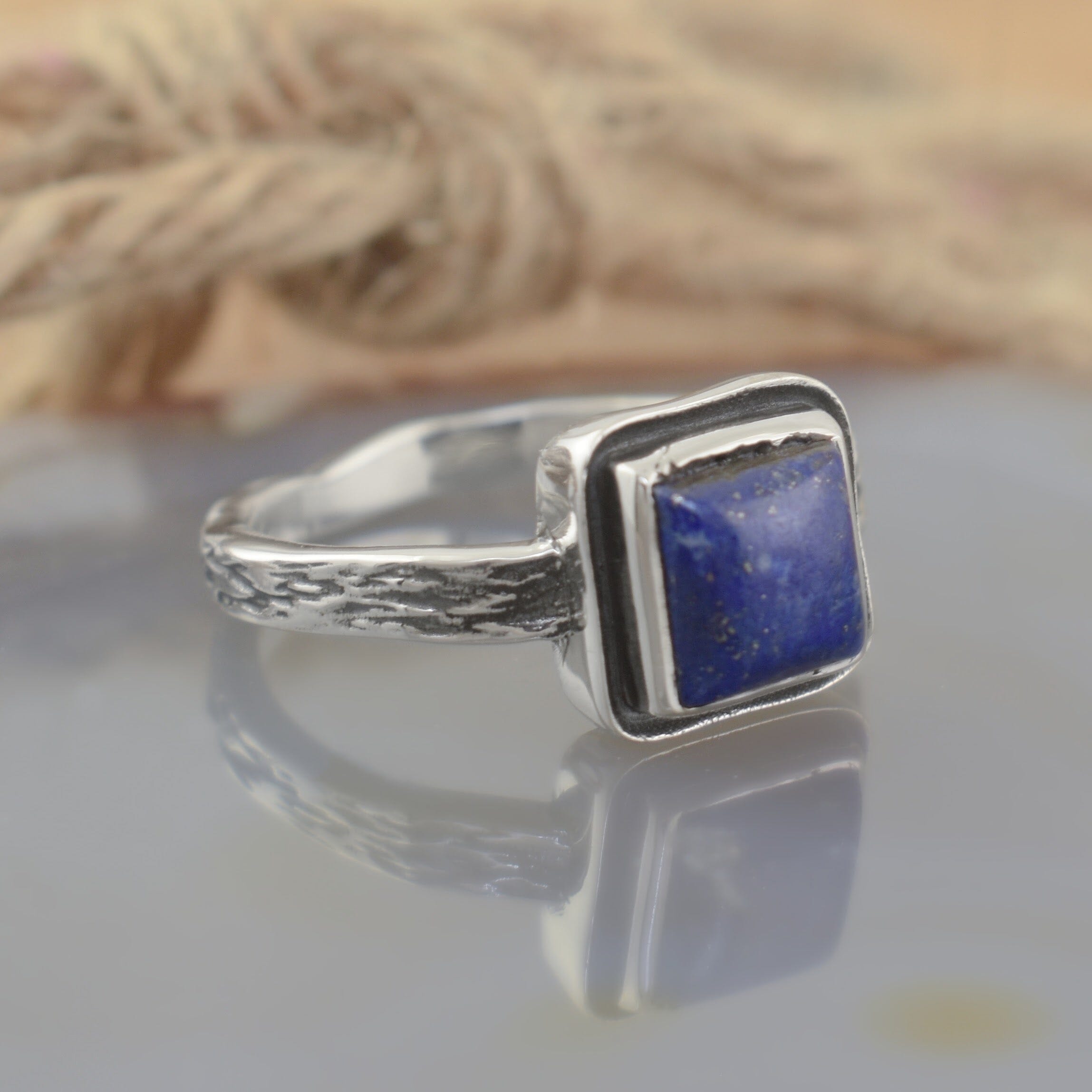 A sterling silver ring with a textured band, featuring a square dark blue stone in the center