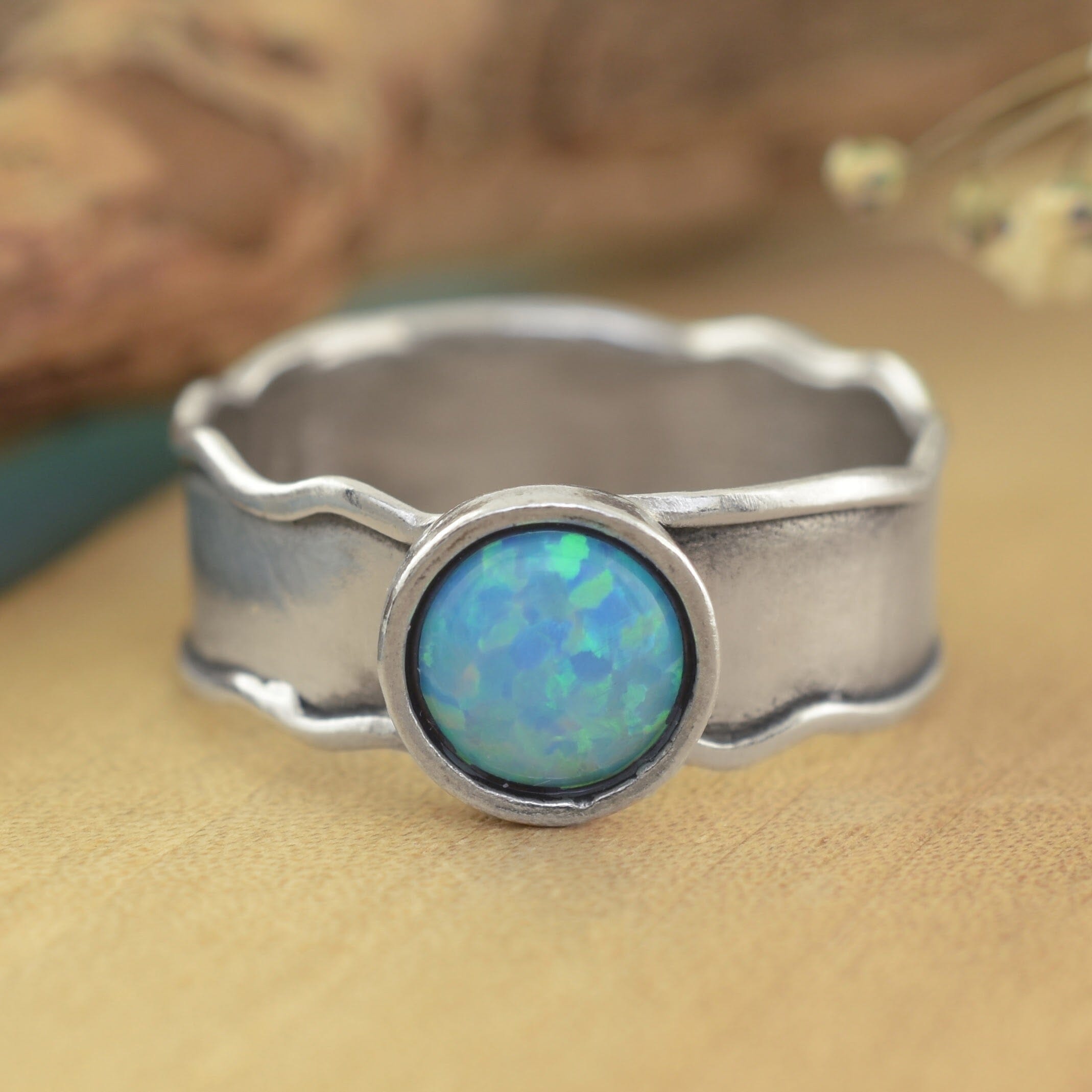 A sterling silver ring with a wavy band and a round cabochon opal gemstone in the center