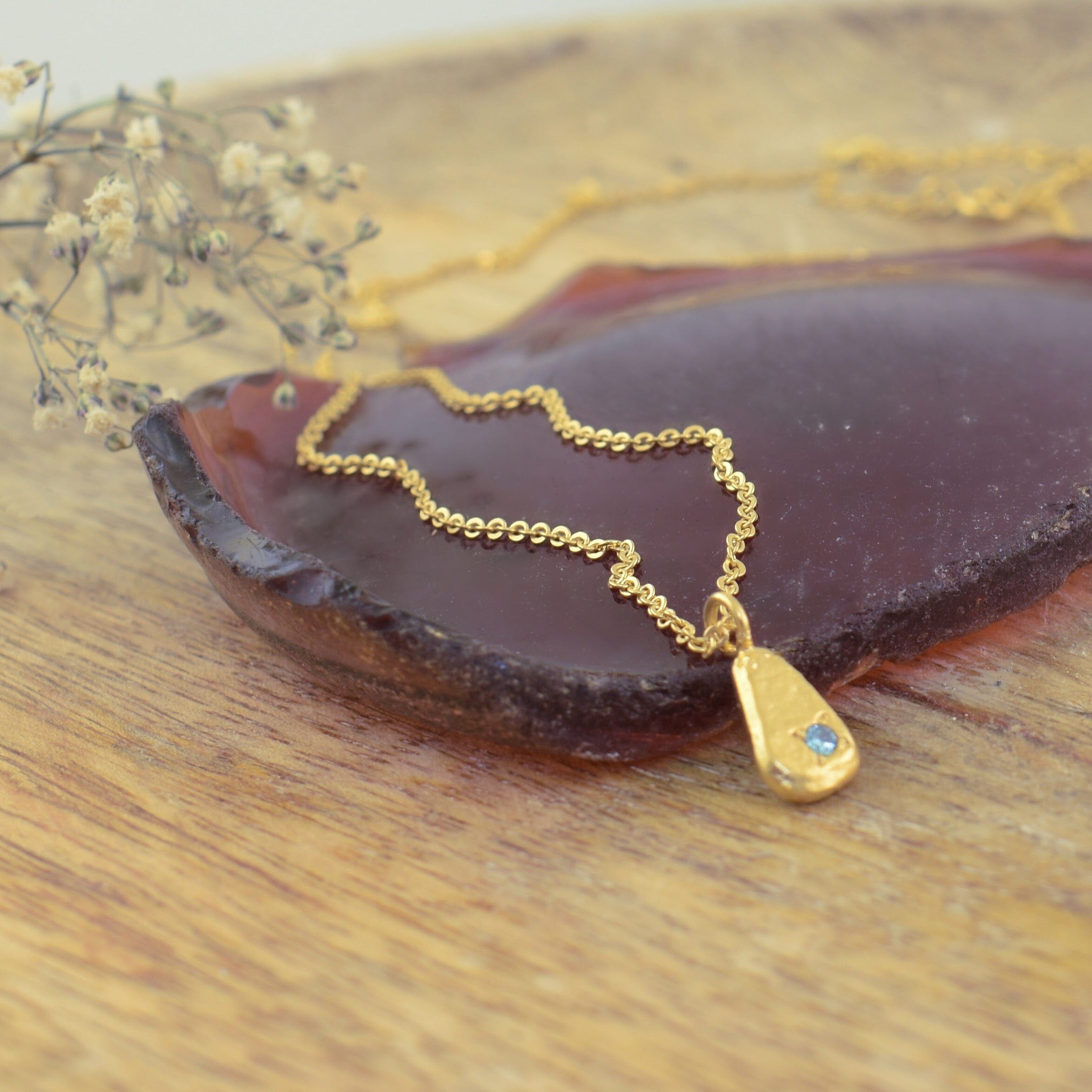 an artisan gold teardrop pendant necklace with a small blue gemstone accent