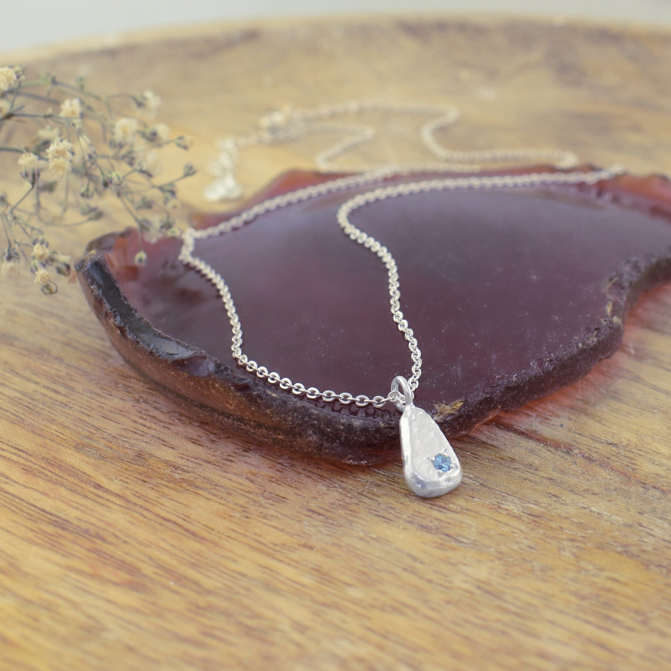 an artisan silver teardrop pendant necklace with a small blue gemstone