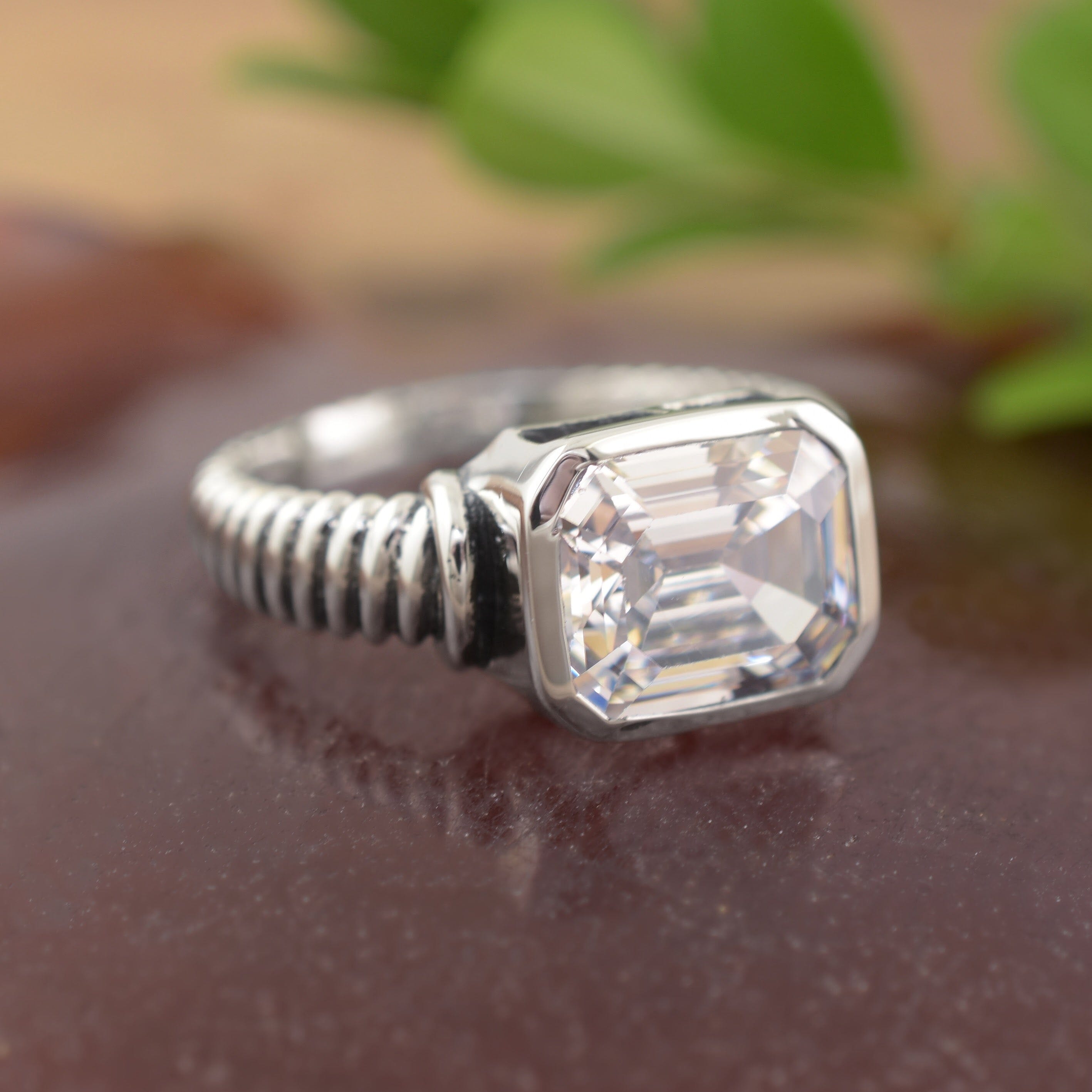 A sterling silver ring with a textured band, featuring a large asscher-cut clear CZ in the center